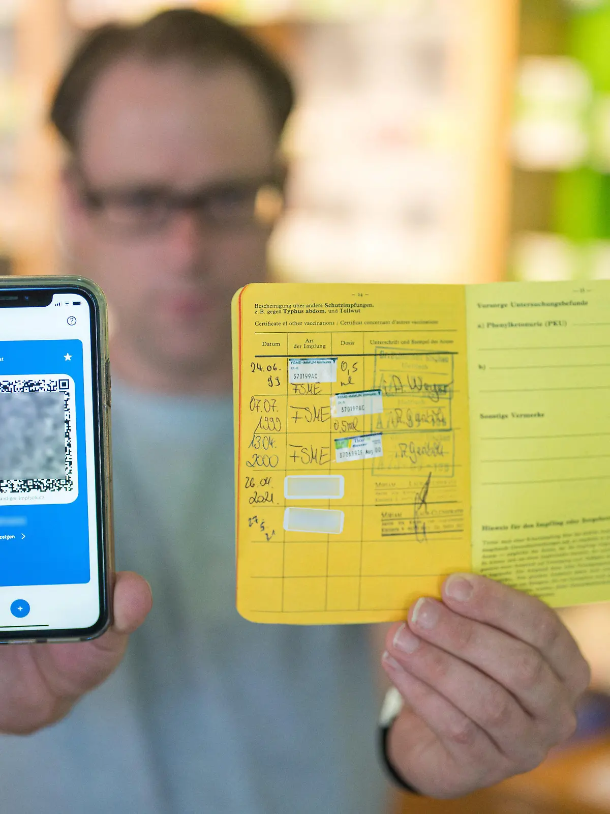 14.06.2021, Saarland, Saarbrücken: Apotheker Stefan Behrens hält ein Smartphone mit dem QR Code eines digitalen Impfausweises und ein Impfbuch in der Hand. Seit heute dürfen Apotheker den digitalen Impfausweis ausstellen. Foto: Oliver Dietze/dpa - ACHTUNG: Die Chargennummern des Coronaimpfstoffes wurden aus rechtlichen Gründen gepixelt +++ dpa-Bildfunk +++