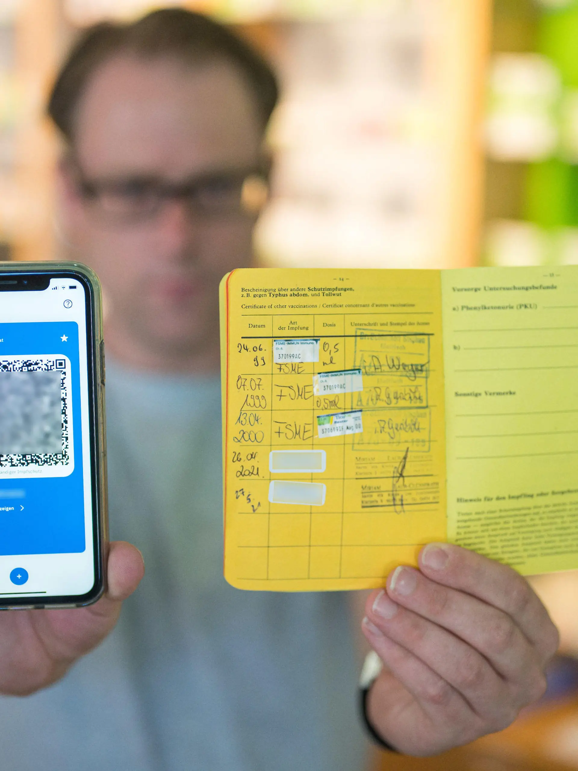 14.06.2021, Saarland, Saarbrücken: Apotheker Stefan Behrens hält ein Smartphone mit dem QR Code eines digitalen Impfausweises und ein Impfbuch in der Hand. Seit heute dürfen Apotheker den digitalen Impfausweis ausstellen. Foto: Oliver Dietze/dpa - ACHTUNG: Die Chargennummern des Coronaimpfstoffes wurden aus rechtlichen Gründen gepixelt +++ dpa-Bildfunk +++