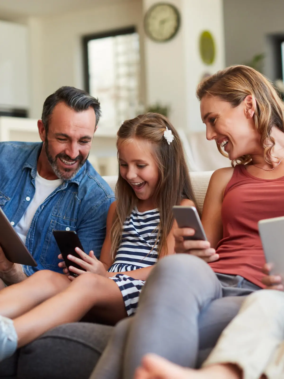 Eine glückliche Familie nutzt mobile Geräte auf dem Sofa.
