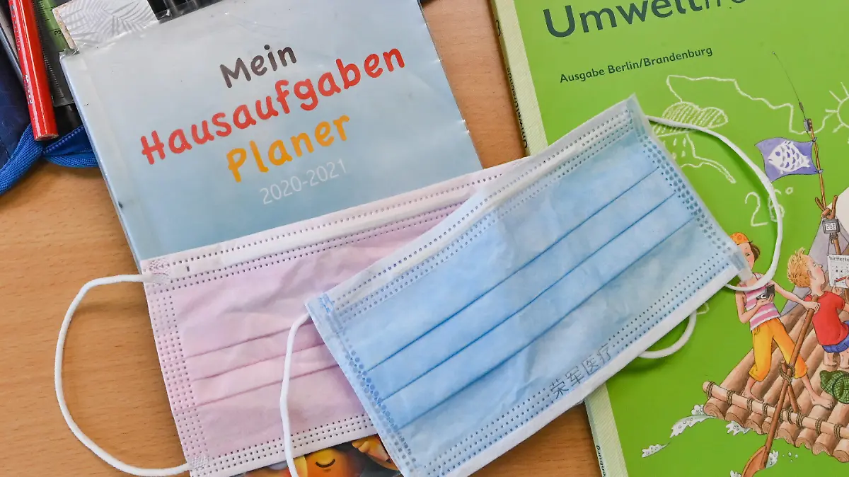 28.05.2021, Brandenburg, Frankfurt (Oder): Masken liegen während einer Pause auf Arbeitsmaterialien eines Schülers in einem Klassenraum einer Grundschule. Am Montag (31. Mai) kehren die Grundschulen in Brandenburg nach dem Kabinettsbeschluss vollständig wieder in den Präsenzunterricht zurück, eine Woche später die weiterführenden Schulen (7. Juni). Voraussetzung dafür ist ein Wert von weniger als 50 Neuinfektionen je 100 000 Einwohner binnen sieben Tagen in dem Landkreis, und zwar an drei Tagen in Folge. Dies war nach Woidkes Angaben am Dienstag in zwei Dritteln der Kreise und kreisfreien Städte der Fall. Die Maskenpflicht drinnen und draußen bleibt bestehen, auch die Testpflicht. Ohne Nachweis gibt es Distanzunterricht. Foto: Patrick Pleul/dpa-Zentralbild/ZB +++ dpa-Bildfunk +++
