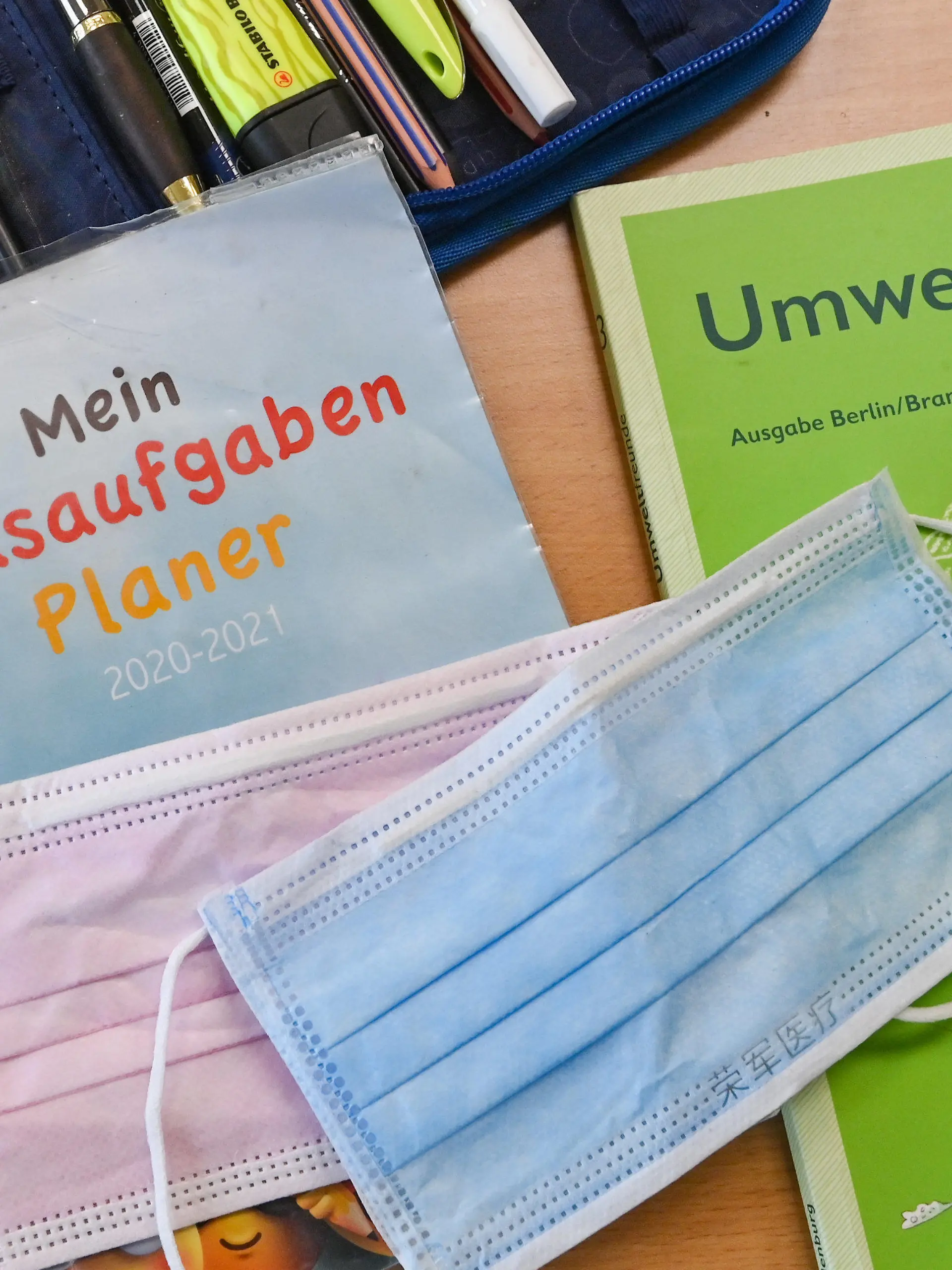 28.05.2021, Brandenburg, Frankfurt (Oder): Masken liegen während einer Pause auf Arbeitsmaterialien eines Schülers in einem Klassenraum einer Grundschule. Am Montag (31. Mai) kehren die Grundschulen in Brandenburg nach dem Kabinettsbeschluss vollständig wieder in den Präsenzunterricht zurück, eine Woche später die weiterführenden Schulen (7. Juni). Voraussetzung dafür ist ein Wert von weniger als 50 Neuinfektionen je 100 000 Einwohner binnen sieben Tagen in dem Landkreis, und zwar an drei Tagen in Folge. Dies war nach Woidkes Angaben am Dienstag in zwei Dritteln der Kreise und kreisfreien Städte der Fall. Die Maskenpflicht drinnen und draußen bleibt bestehen, auch die Testpflicht. Ohne Nachweis gibt es Distanzunterricht. Foto: Patrick Pleul/dpa-Zentralbild/ZB +++ dpa-Bildfunk +++