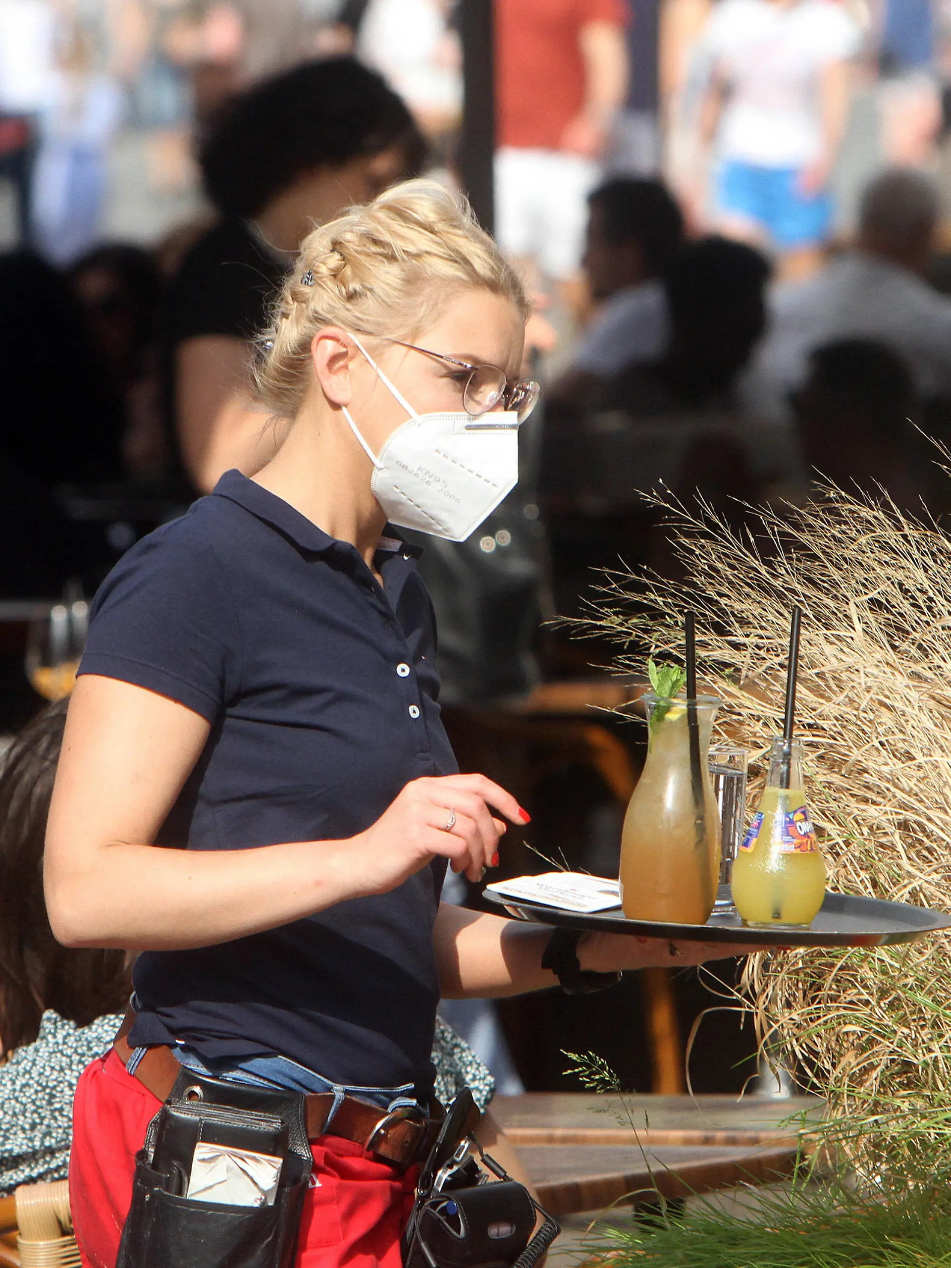Aufgrund anhaltend niedriger Inzidenzen in Würzburg dürfen gastronomische Betriebe ihren Außenbereich auch ohne negativen Coronatest wieder öffnen. Eine Kellnerin eines Restaurants in der Innenstadt liefert auf ihrem Tablett Getränke an Gäste an einem vollbesetzten Tisch, Bayern, Deutschland *** Due to persistently low incidences in Würzburg, gastronomic establishments are allowed to reopen their outdoor areas even without a negative coronatest A waitress at a downtown restaurant delivers drinks on her tray to patrons at a crowded table, Bavaria, Germany 