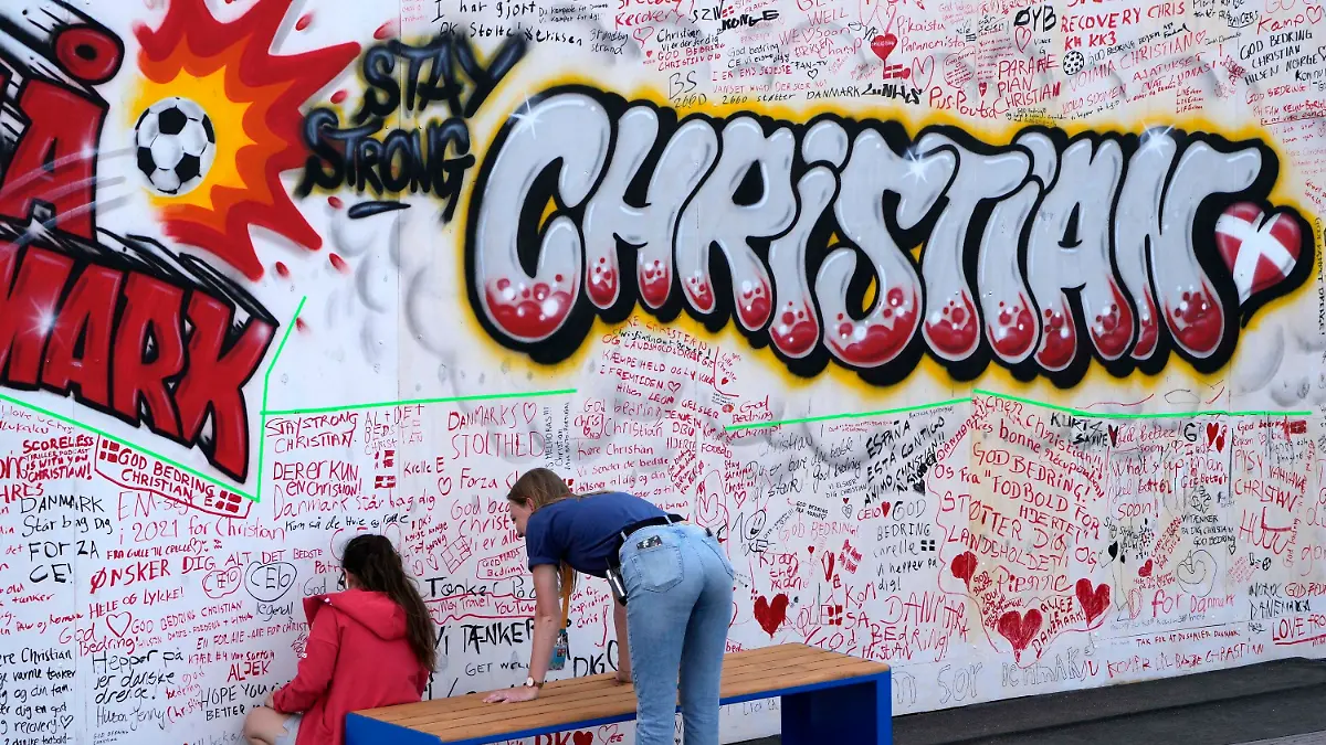 People leave well wishes at a graffiti for Danish player Christian Eriksen on a wall at the fanzone in Copenhagen, Denmark, Monday, June 14, 2021. Eriksen remains in hospital after he collapsed on the pitch during the European Championship game against Finland on Saturday and needed CPR from medical staff before regaining consciousness. (AP Photo/Martin Meissner)