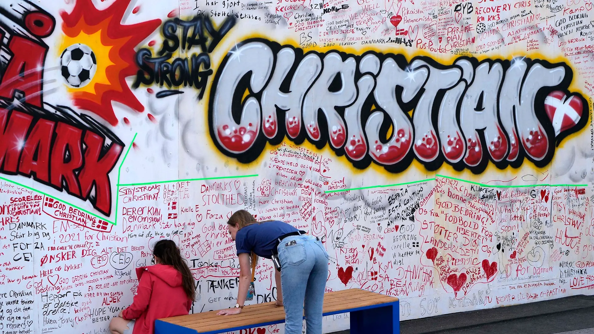 People leave well wishes at a graffiti for Danish player Christian Eriksen on a wall at the fanzone in Copenhagen, Denmark, Monday, June 14, 2021. Eriksen remains in hospital after he collapsed on the pitch during the European Championship game against Finland on Saturday and needed CPR from medical staff before regaining consciousness. (AP Photo/Martin Meissner)