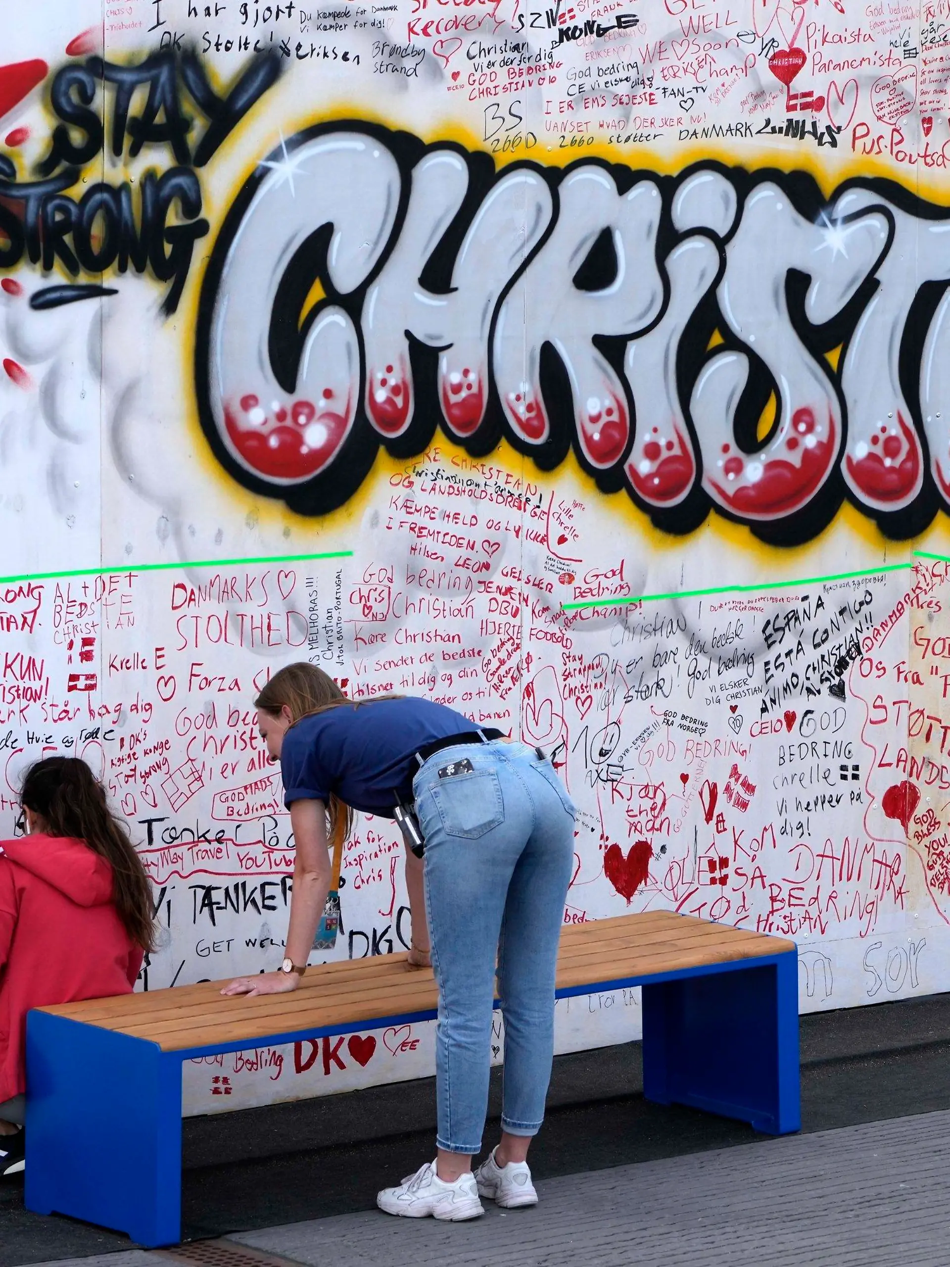 People leave well wishes at a graffiti for Danish player Christian Eriksen on a wall at the fanzone in Copenhagen, Denmark, Monday, June 14, 2021. Eriksen remains in hospital after he collapsed on the pitch during the European Championship game against Finland on Saturday and needed CPR from medical staff before regaining consciousness. (AP Photo/Martin Meissner)