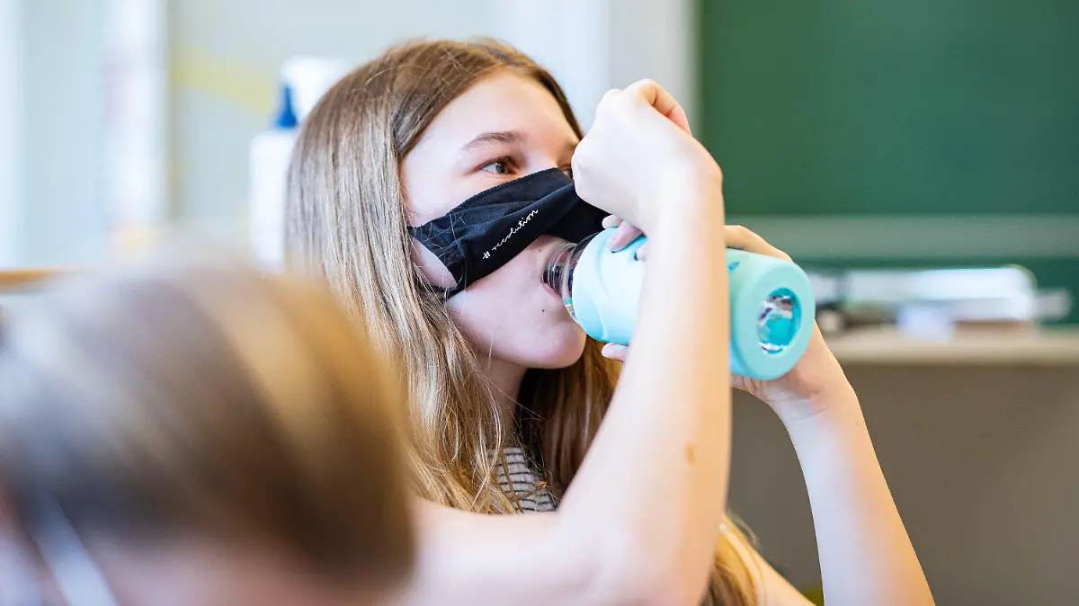 12.08.2020, Nordrhein-Westfalen, Münster: Eine Schülerin der Klasse 8a der Gesamtschule in Münster, hebt ihre Mund- und Nasenmaske an um etwas zu trinken. Das Bundesland Nordrhein-Westfalen startet mit Maskenpflicht nach den Sommerferien wieder in den Regel-Schulbetrieb. Foto: Guido Kirchner/dpa +++ dpa-Bildfunk +++