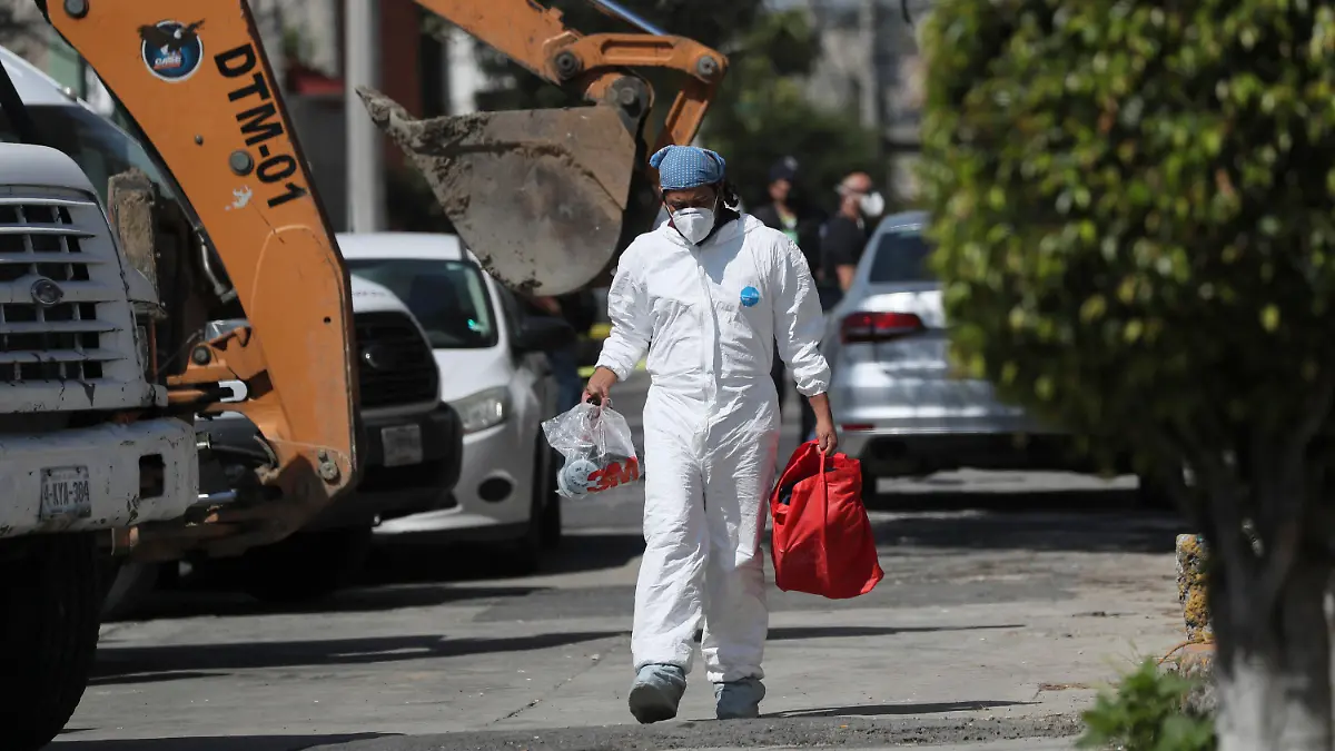 A forensic investigator carries equipment outside the house where police found bones under the floor in the Atizapan municipality of the State of Mexico, Thursday, May 20, 2021. Police have turned up bones and other evidence under the floor of the house where a man was arrested for allegedly stabbing a woman to death and hacking up her body. (AP Photo/Fernando Llano)