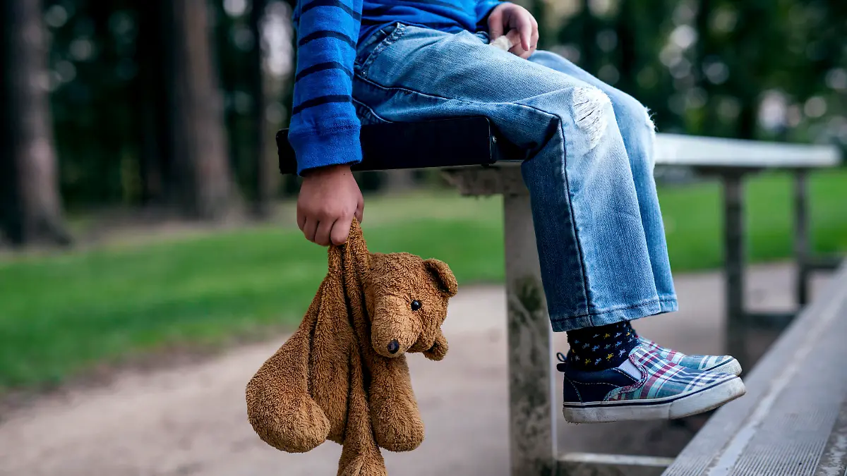 Young boy holding teddybear while alone on the bleachers
