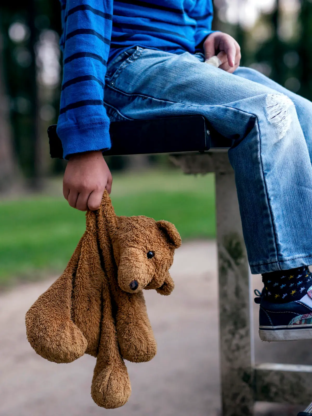 Young boy holding teddybear while alone on the bleachers