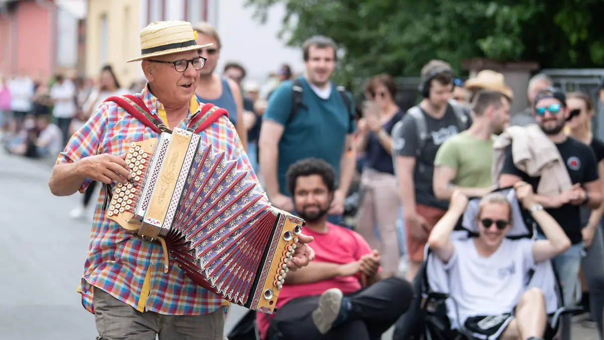 12.06.2021, Hessen, Babenhausen: Mit einer spontanen musikalischen Einlage unterhält Harmonika-Spieler Norbert Herbert - Künstlername ·Happy-Man· - Impfwillige, die in einer mehrer hundert Meter langen Schlange vor einer Arztpraxis auf ihre Corona-Schutzimpfung warten. Ein Hausarzt hatte zu einem ·offenen Impftag· aufgerufen. Tausende Menschen waren daraufhin in die Innenstadt von Babenhausen gekommen um eine von 1000 Impfdosen zu ergattern. Foto: Boris Roessler/dpa +++ dpa-Bildfunk +++