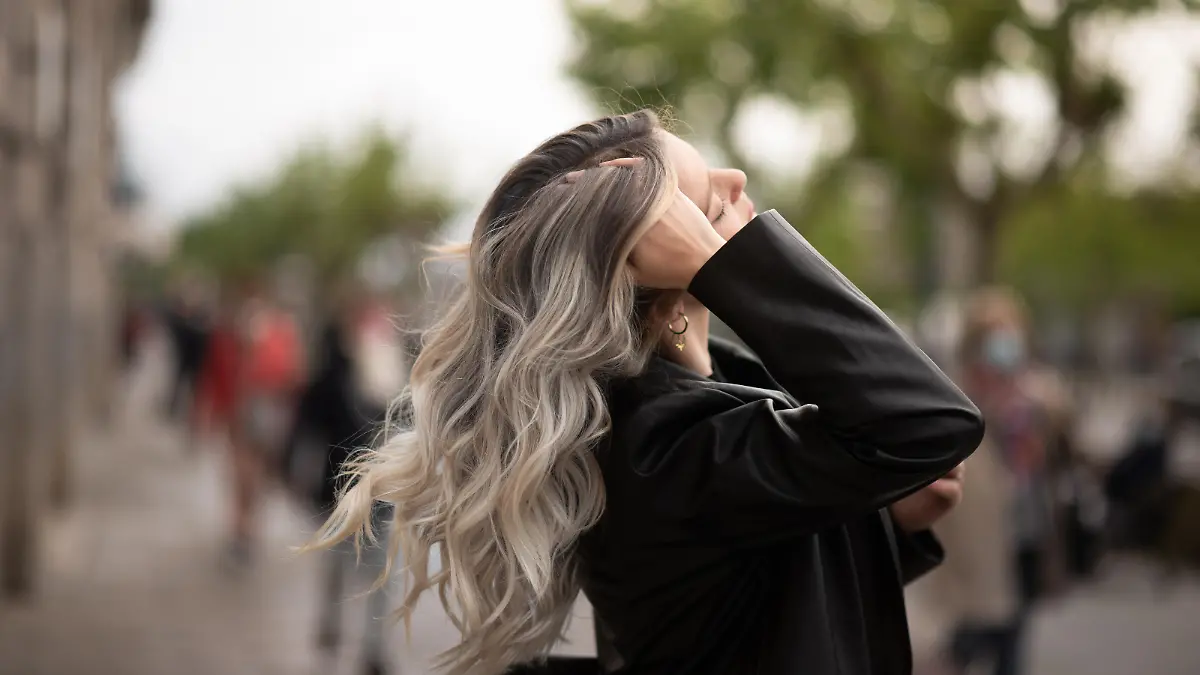 Eine junge Frau schwingt im Wind ihre Haarmähne hin und her. Die Haare sind leicht gelockt bzw. gewellt und haben verschiedene Farbnuancen.