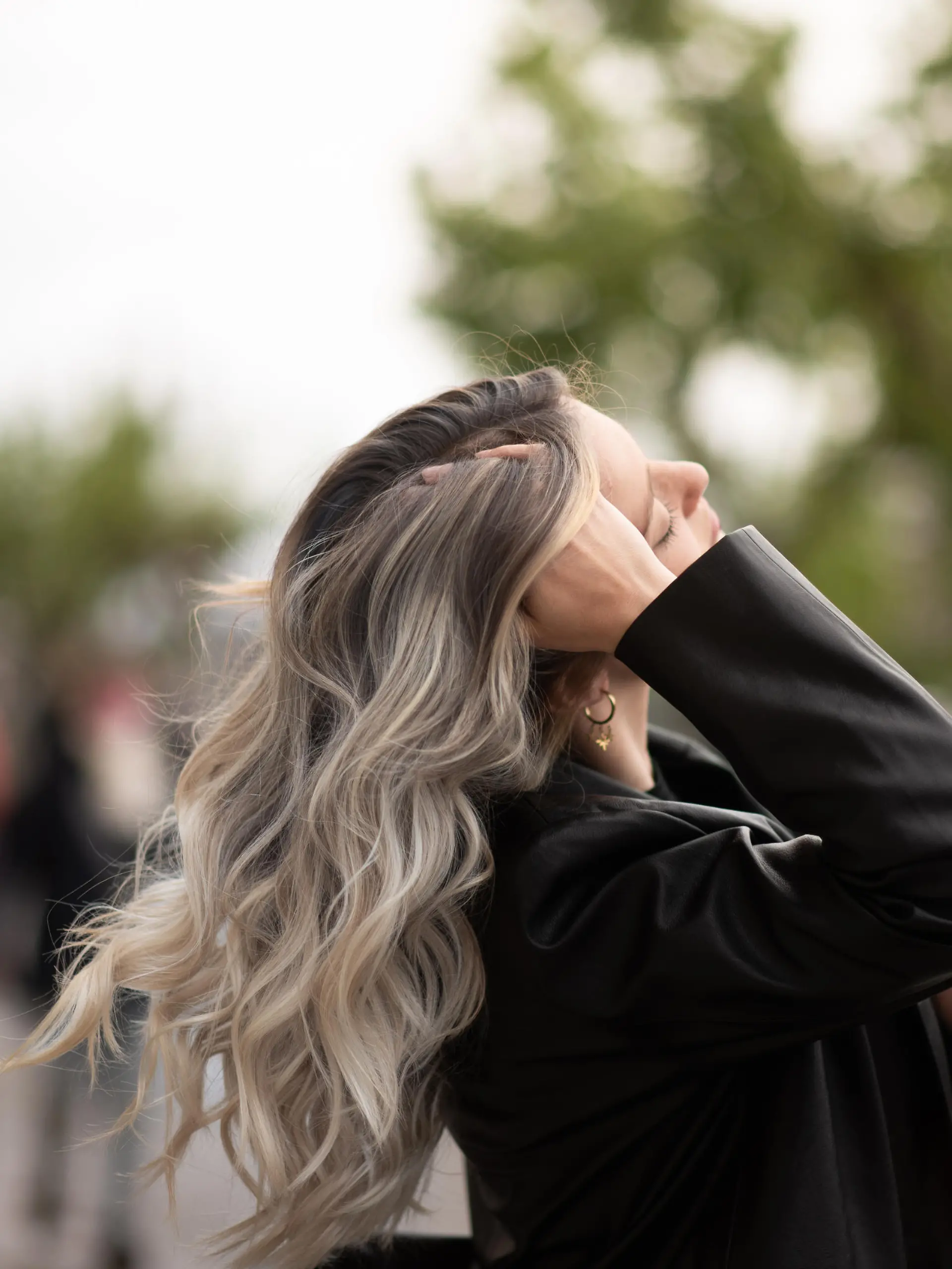 Eine junge Frau schwingt im Wind ihre Haarmähne hin und her. Die Haare sind leicht gelockt bzw. gewellt und haben verschiedene Farbnuancen.