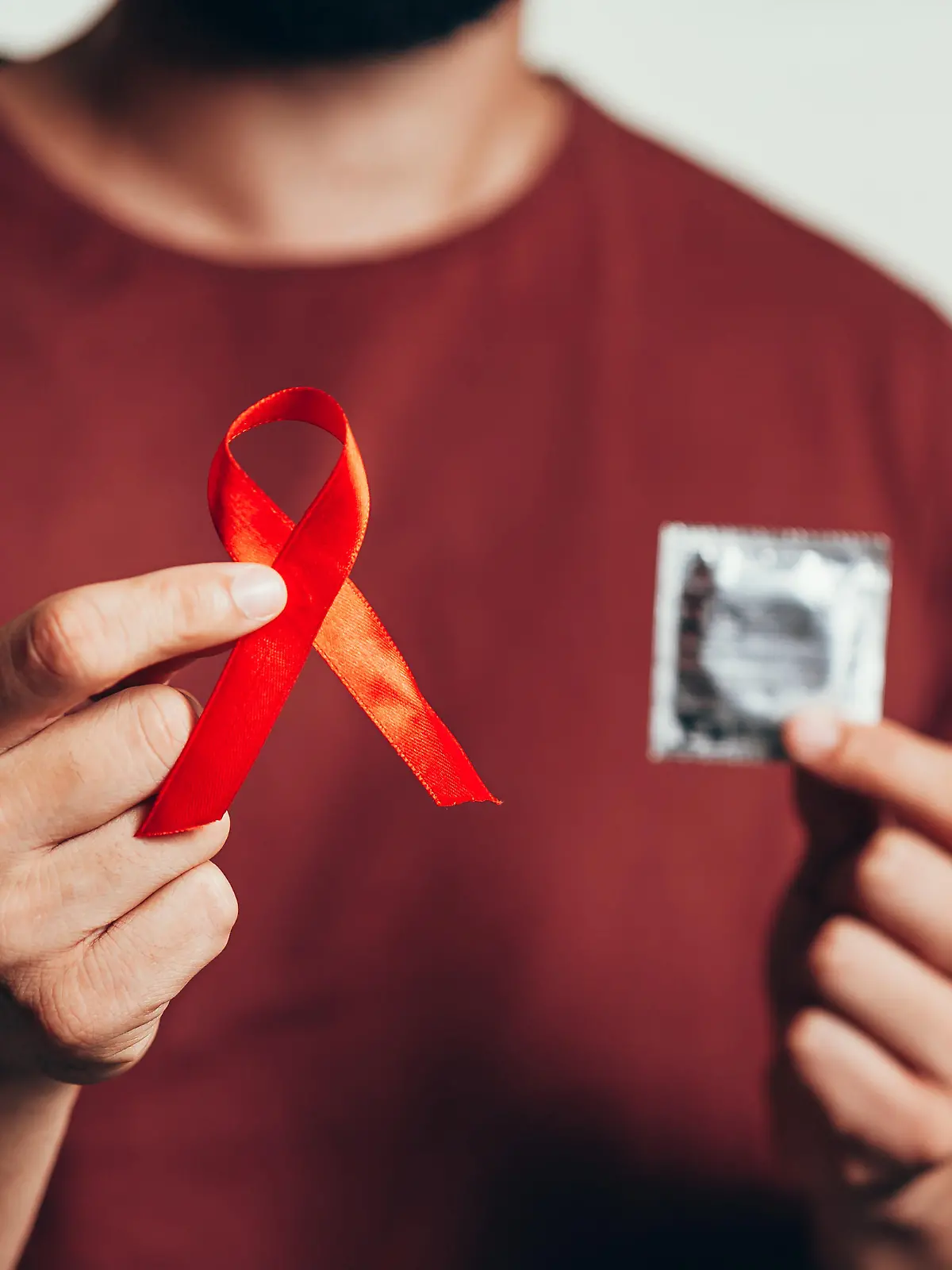 Ein Mann hält in der einen Hand ein Kondom, in der anderen eine rote Schleife, die für die Aufklärung der Krankheit HIV steht.
