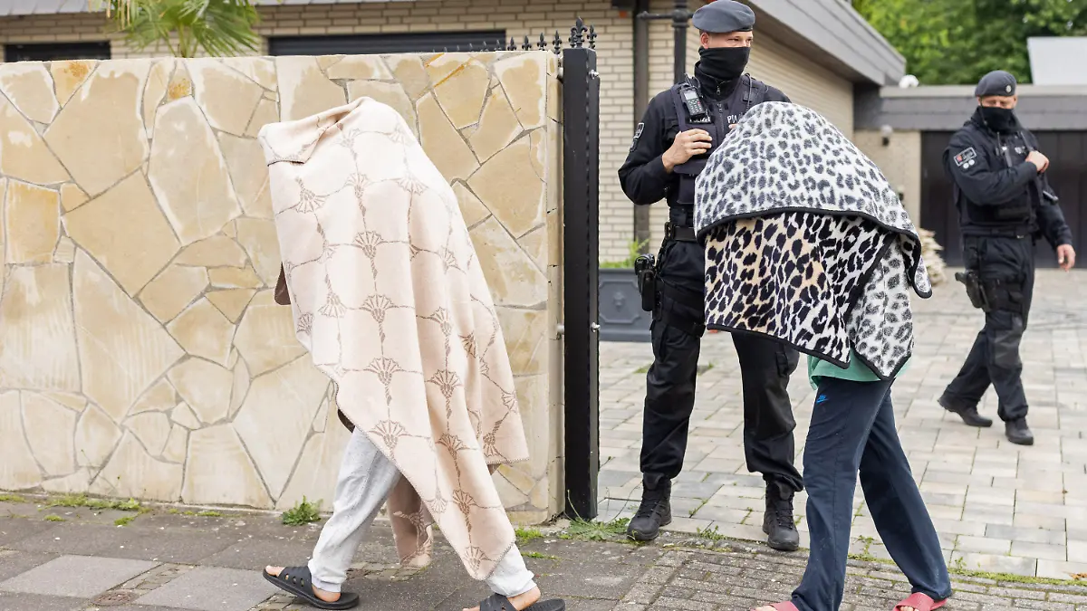 dpatopbilder - 08.06.2021, Nordrhein-Westfalen, Leverkusen: Polizisten stehen vor einer Villa, während zwei Personen mit Decken über dem Oberkörper das Gelände verlassen. Bei Ermittlungen gegen Clankriminalität durchsuchten Spezialkräfte der Polizei rund 30 Objekte in Nordrhein-Westfalen. Foto: Marcel Kusch/dpa +++ dpa-Bildfunk +++