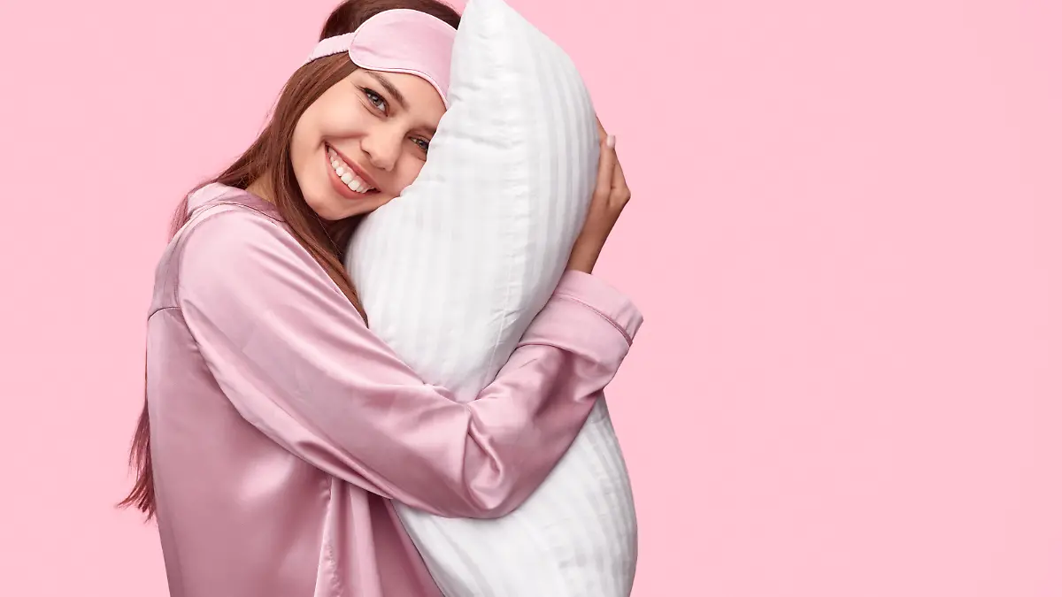 Eine junge Frau im Pyjama und mit einer Schlafmaske auf dem Kopf schaut seitlich und grinsend in die Kamera.