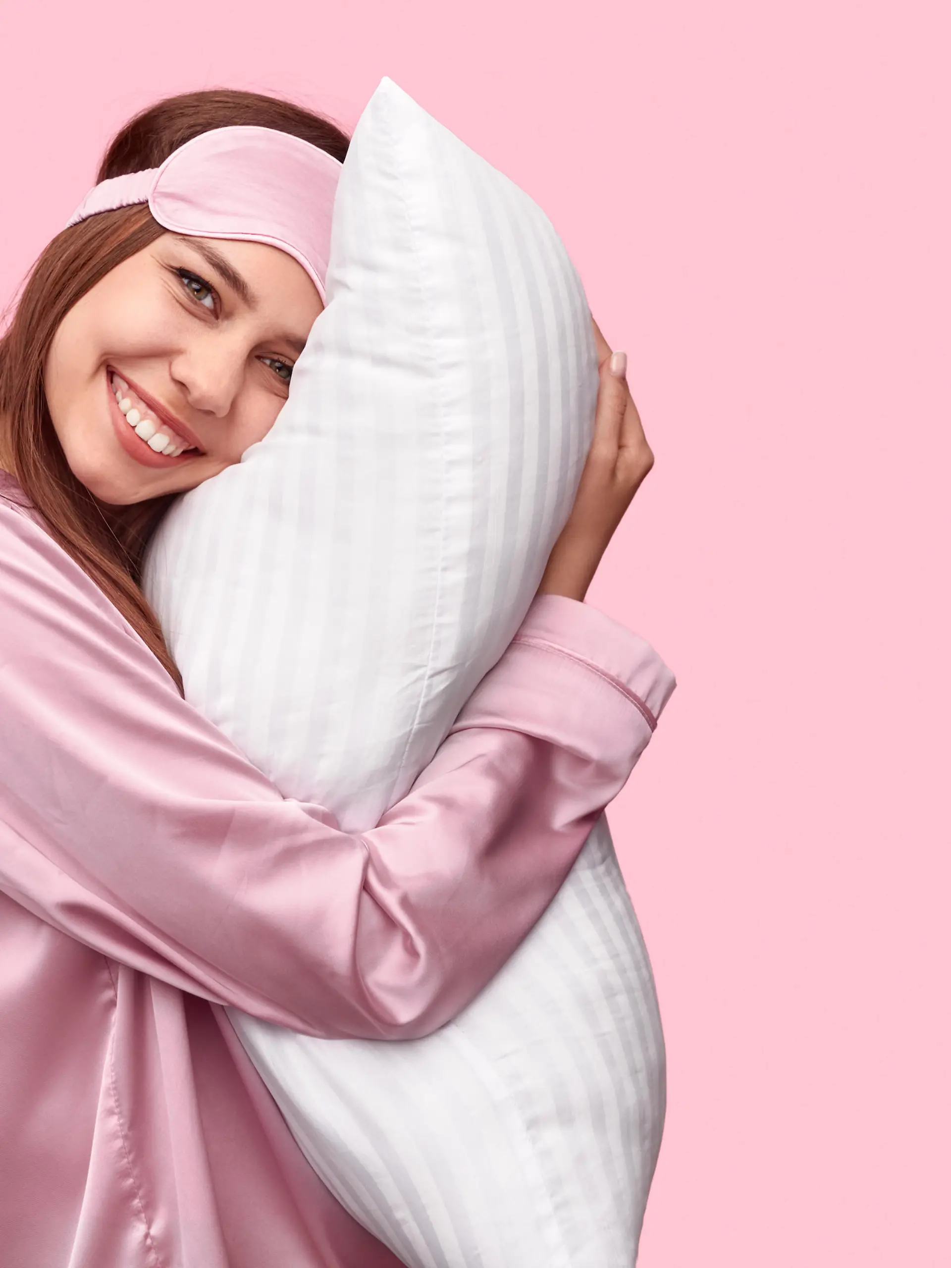Eine junge Frau im Pyjama und mit einer Schlafmaske auf dem Kopf schaut seitlich und grinsend in die Kamera.