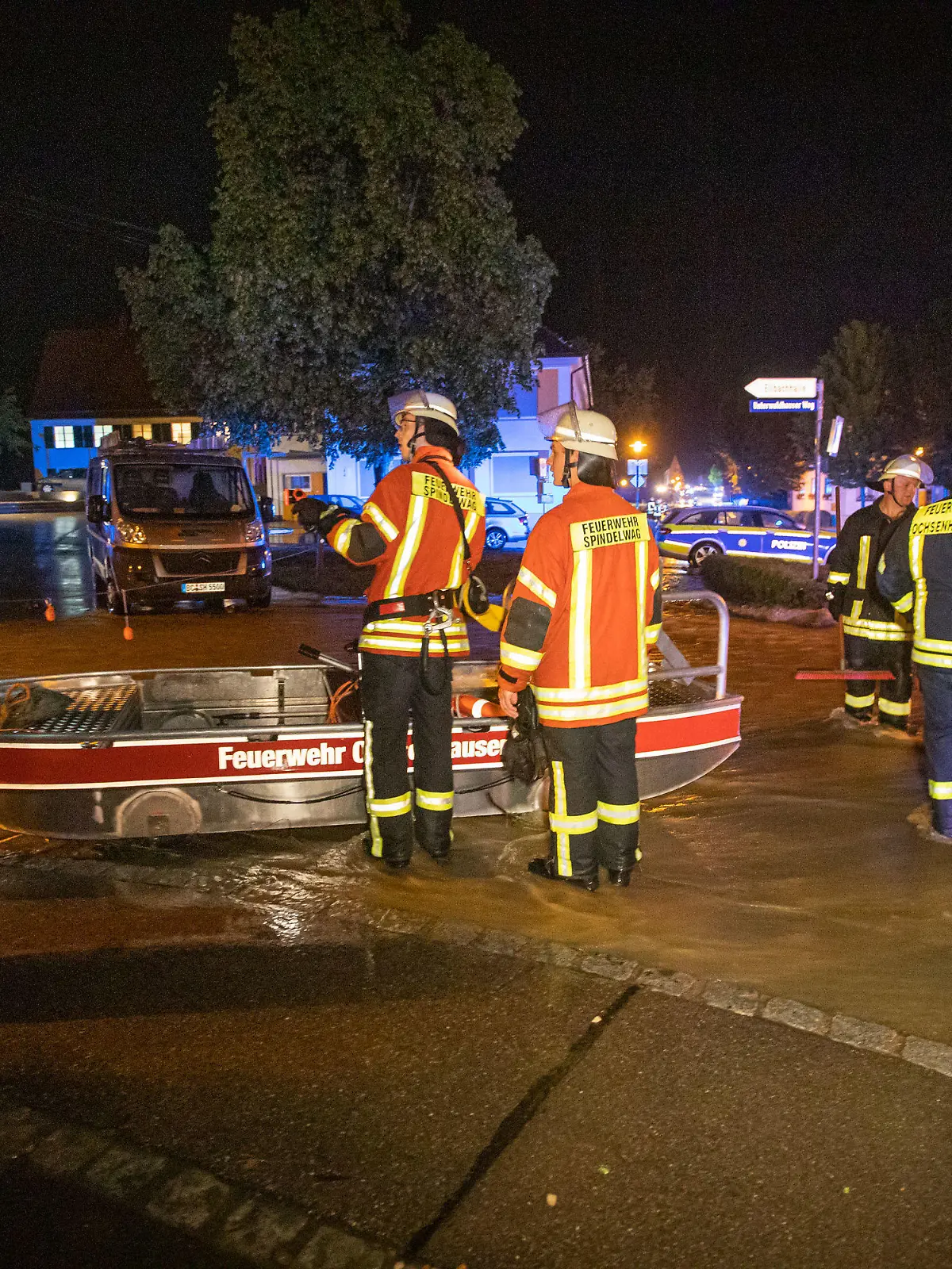 07.06.2021, Baden-Württemberg, Rot an der Rot: Feuerwehrleute stehen neben einem Feuerwehrboot auf einer Straße in den Fluten eines heftigen Unwetters. Ein Mann war bei den heftigen Regenfällen in seiner Wohnung im Untergeschoss eines Mehrfamilienhauses ertrunken.    (zu dpa "Mann wird in Wohnung von Wassermassen überrascht und ertrinkt") Foto: Simon Adomat/VMD Images/dpa +++ dpa-Bildfunk +++