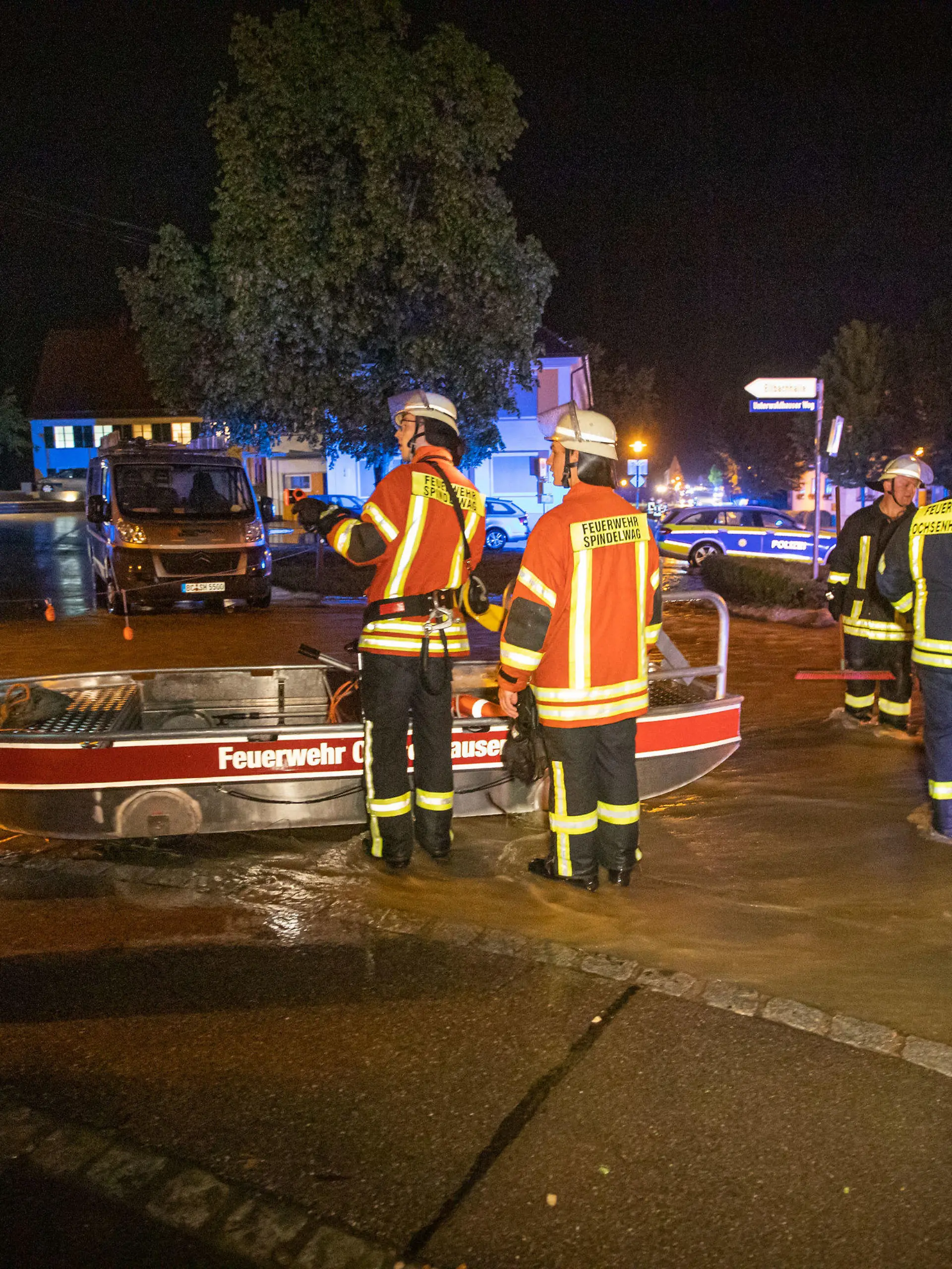 07.06.2021, Baden-Württemberg, Rot an der Rot: Feuerwehrleute stehen neben einem Feuerwehrboot auf einer Straße in den Fluten eines heftigen Unwetters. Ein Mann war bei den heftigen Regenfällen in seiner Wohnung im Untergeschoss eines Mehrfamilienhauses ertrunken.    (zu dpa "Mann wird in Wohnung von Wassermassen überrascht und ertrinkt") Foto: Simon Adomat/VMD Images/dpa +++ dpa-Bildfunk +++