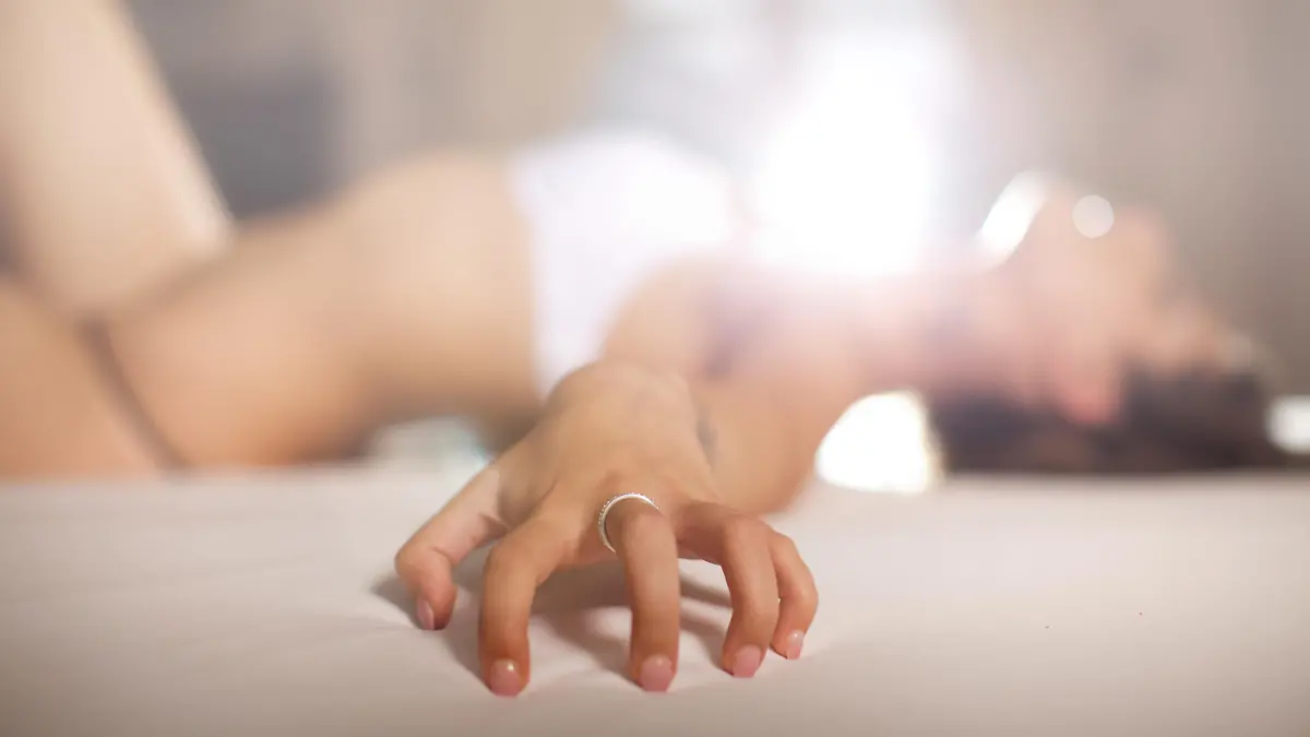 Frau liegt im Bett und hat Orgasmus