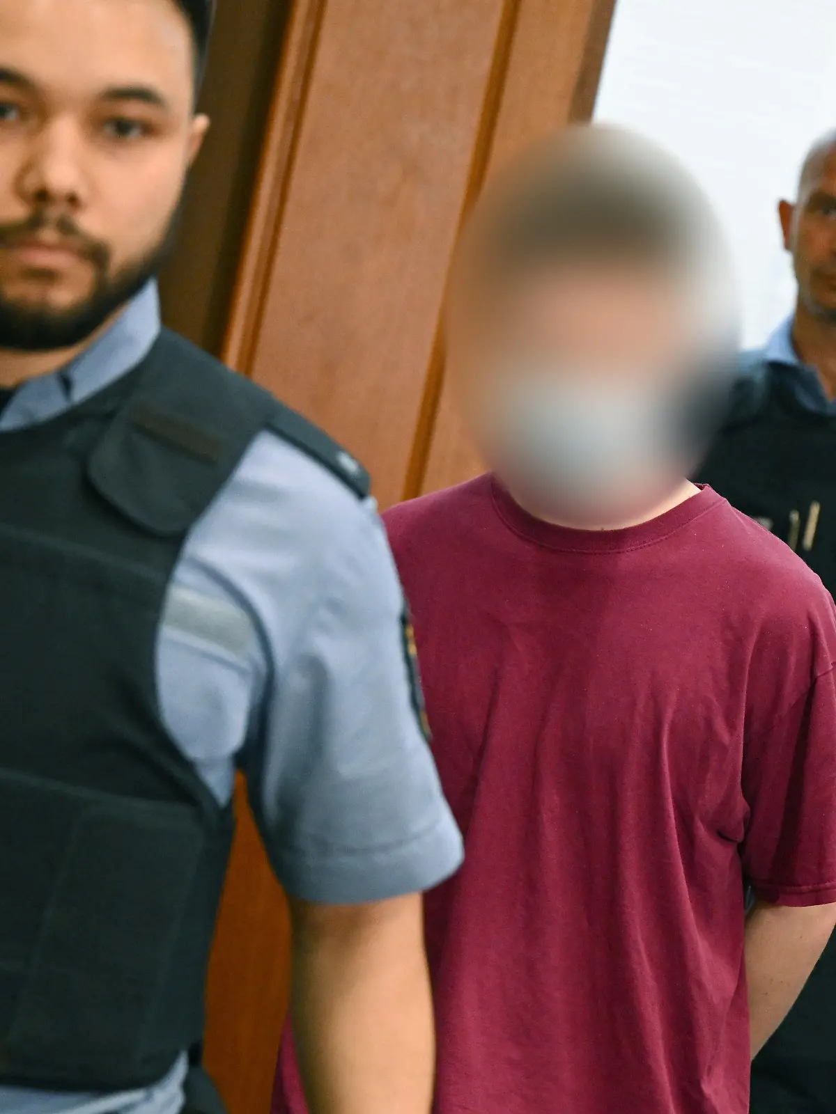 02.08.2022, Hessen, Frankfurt/Main: Der Angeklagte Marvin E. (M) kommt in Begleitung von Justizbeamten zum Prozessauftakt in den Gerichtssaal des Oberlandesgerichts. Die Bundesanwaltschaft wirft dem Mann aus Nordhessen die versuchte Gründung einer terroristischen Vereinigung und die Vorbereitung einer schweren staatsgefährdenden Gewalttat vor. Marvin E. soll aus rechtsextremistischen Motiven Anschläge mit Schusswaffen und Sprengsätzen geplant und vorgehabt haben, eine Terrororganisation zu bilden. Foto: Arne Dedert/dpa - ACHTUNG: Angeklagter auf Anweisung des Gerichts gepixelt! +++ dpa-Bildfunk +++