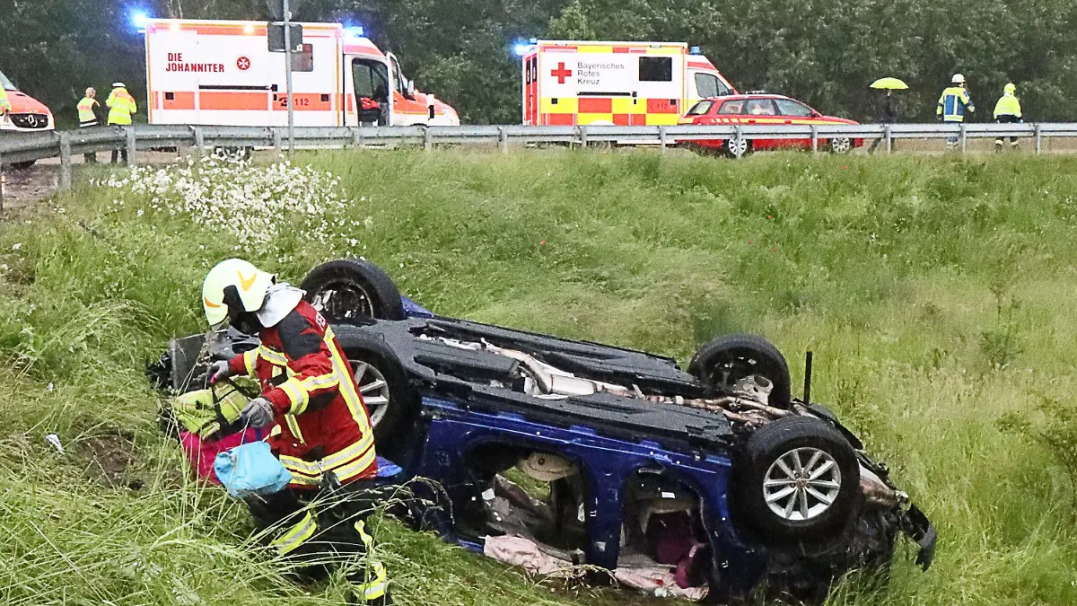 06.06.2021, Baden-Württemberg, Jettingen-Scheppach: Ein Retter holt persönliche Dinge einer Familie aus dem Wrack von deren Fahrzeug an der A8. Das Fahrzeug geriet bei teils schwerem Regen ins Schleudern, kam dann von der Fahrbahn ab, überschlug sich mehrfach und blieb schließlich auf dem Dach liegen. Die Insassen, eine fünfköpfige Familie, darunter drei Kinder, sind verletzt worden. Foto: Mario Obeser/dpa +++ dpa-Bildfunk +++