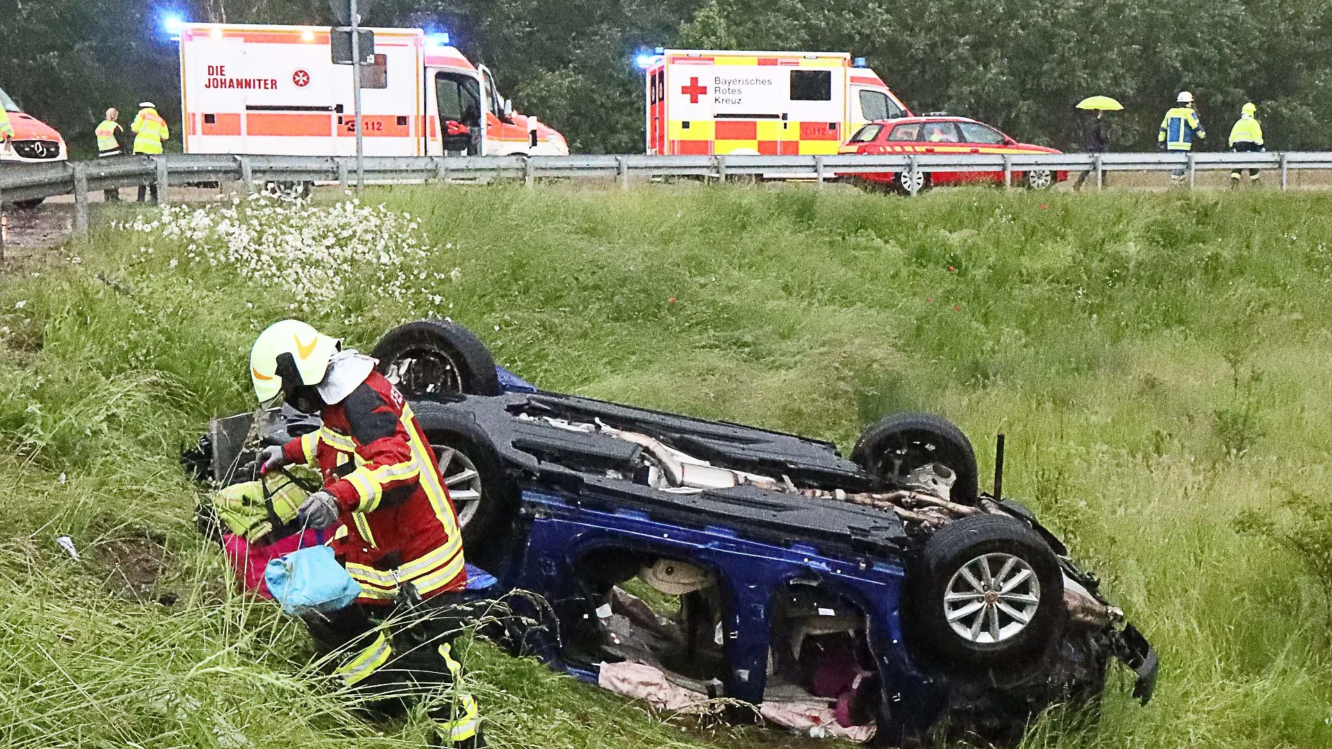 06.06.2021, Baden-Württemberg, Jettingen-Scheppach: Ein Retter holt persönliche Dinge einer Familie aus dem Wrack von deren Fahrzeug an der A8. Das Fahrzeug geriet bei teils schwerem Regen ins Schleudern, kam dann von der Fahrbahn ab, überschlug sich mehrfach und blieb schließlich auf dem Dach liegen. Die Insassen, eine fünfköpfige Familie, darunter drei Kinder, sind verletzt worden. Foto: Mario Obeser/dpa +++ dpa-Bildfunk +++