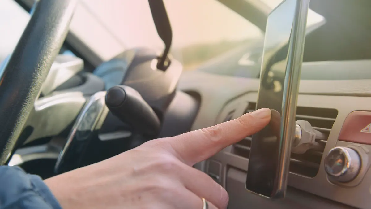 Eine Frau, von der man nur die Hand erkennen kann, benutzt während der Fahrt ihr Handy bzw. mobiles Endgerät.