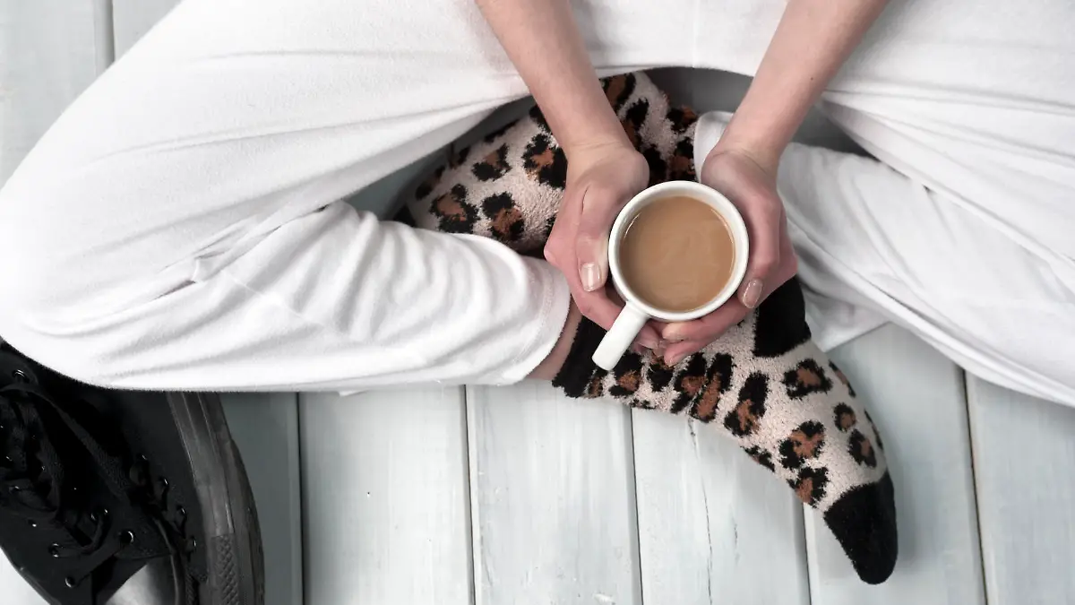 Teenage girl sitting on floor holding a coffee cup. Body part close up on wooden surface
