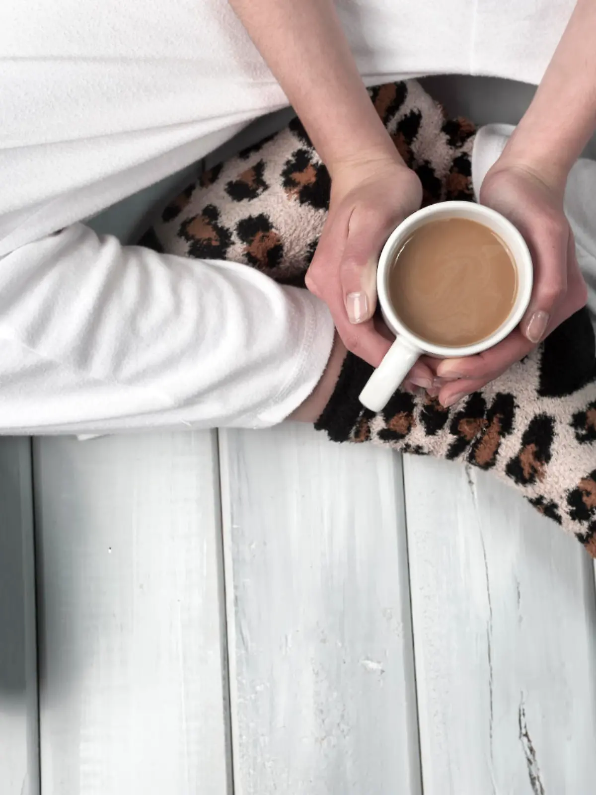 Teenage girl sitting on floor holding a coffee cup. Body part close up on wooden surface