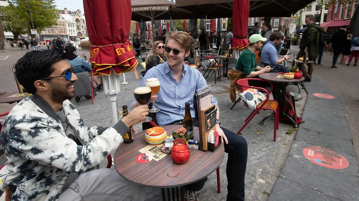 28.04.2021, Niederlande, Utrecht: Männer stoßen auf einer Café-Terrasse an. Die Niederlande haben einige Einschränkungen zur Eindämmung der Corona-Pandemie gelockert und unter anderem Bereiche der Außengastronomie wieder geöffnet. Foto: Peter Dejong/AP/dpa +++ dpa-Bildfunk +++
