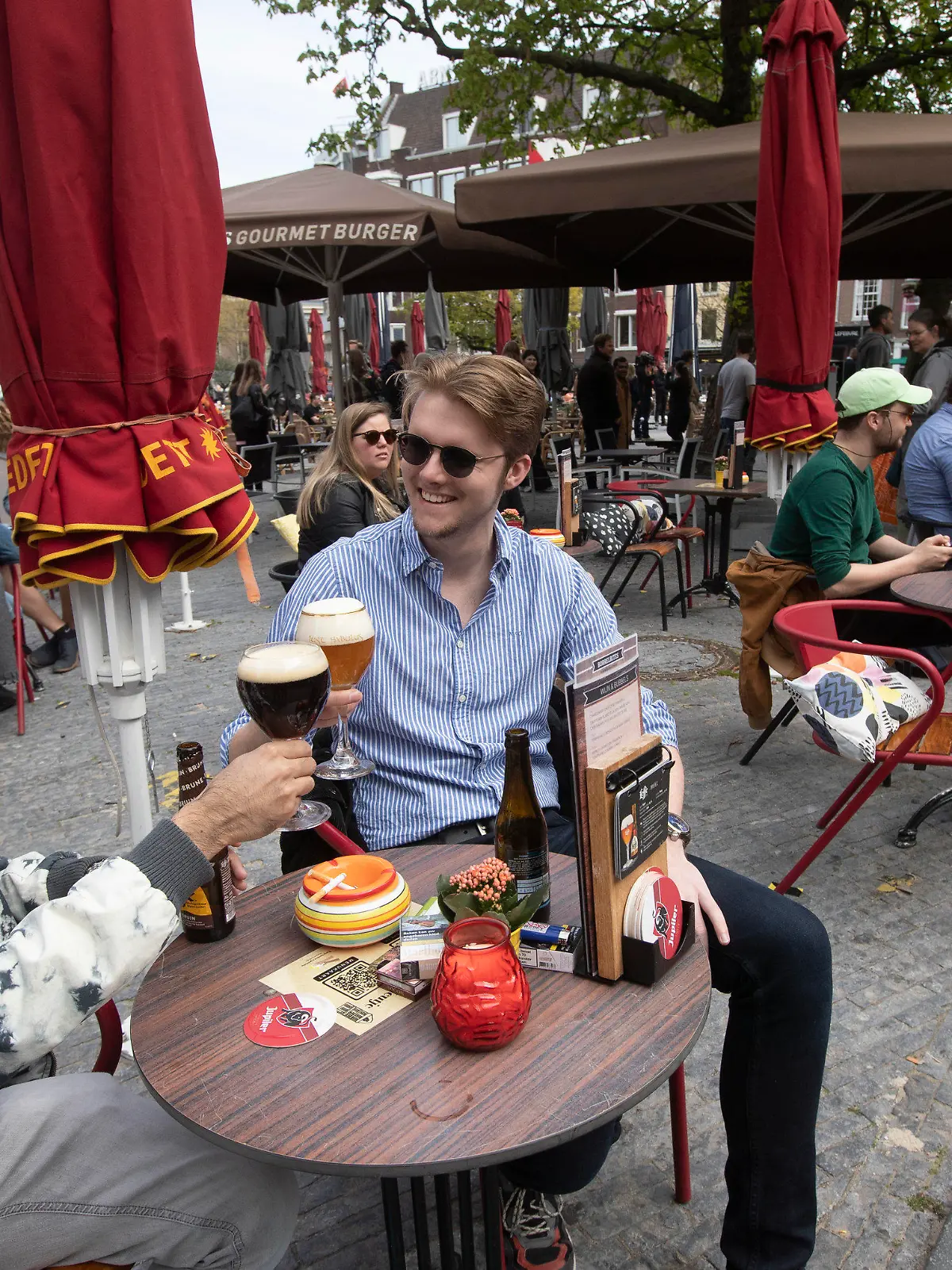 28.04.2021, Niederlande, Utrecht: Männer stoßen auf einer Café-Terrasse an. Die Niederlande haben einige Einschränkungen zur Eindämmung der Corona-Pandemie gelockert und unter anderem Bereiche der Außengastronomie wieder geöffnet. Foto: Peter Dejong/AP/dpa +++ dpa-Bildfunk +++