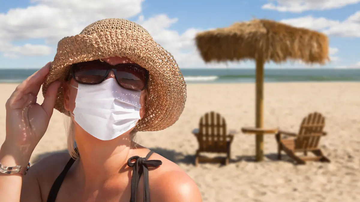 Eine Frau trägt am Strand eine Maske und eine Sonnenbrille.