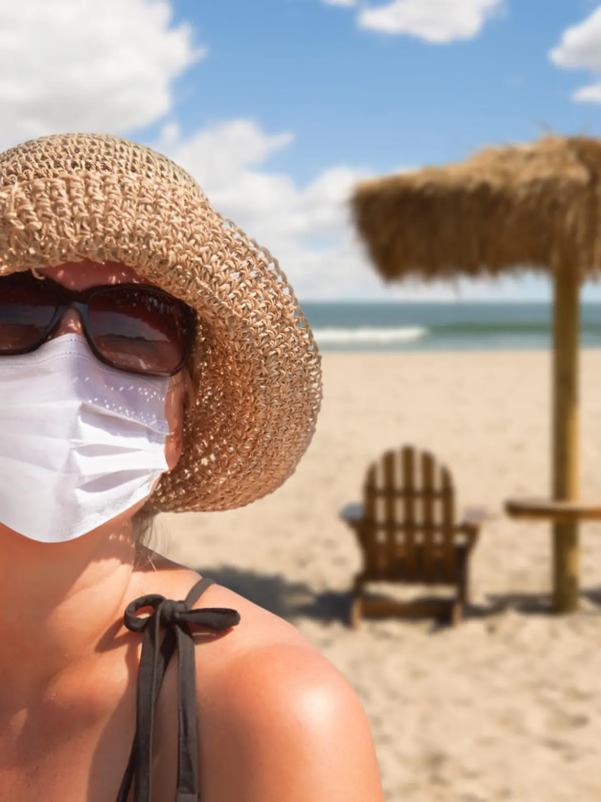 Eine Frau trägt am Strand eine Maske und eine Sonnenbrille.