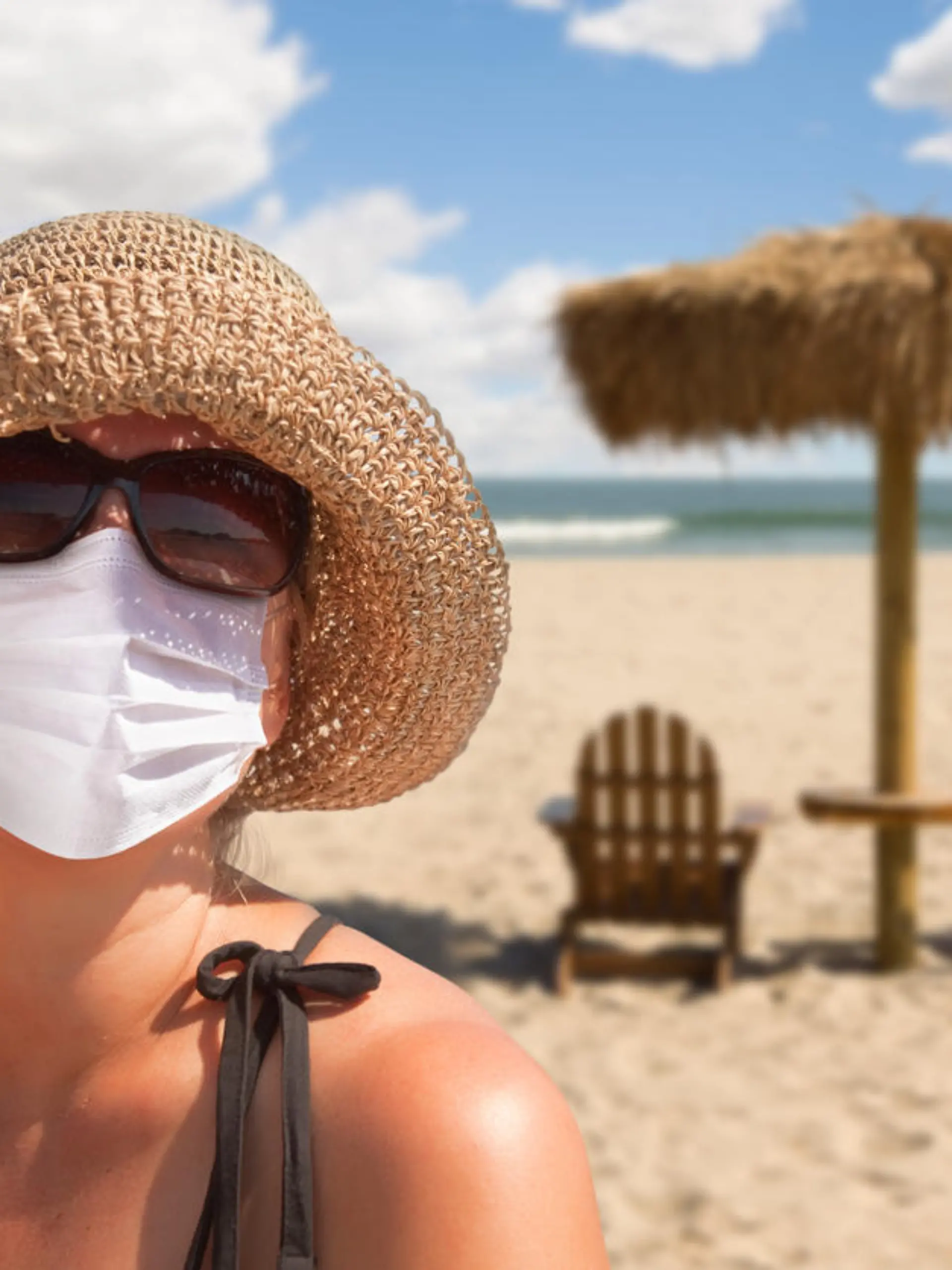 Eine Frau trägt am Strand eine Maske und eine Sonnenbrille.