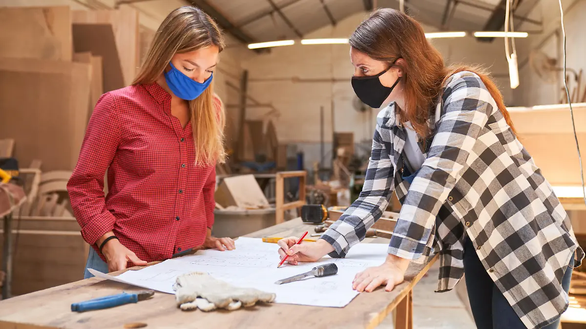 Zwei Handwerker-Frauen mit Mundschutz vor einem Bauplan.