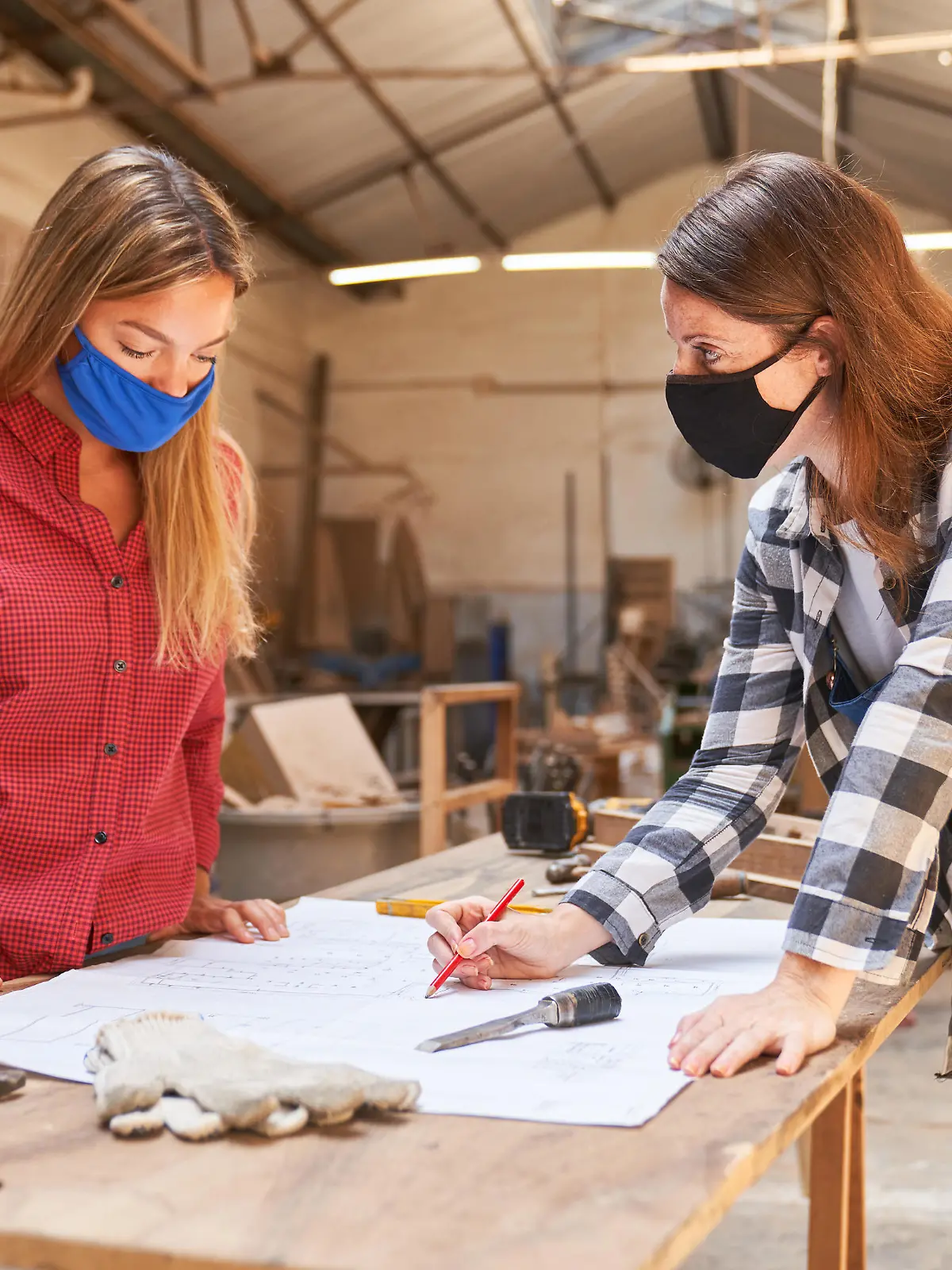 Zwei Handwerker-Frauen mit Mundschutz vor einem Bauplan.