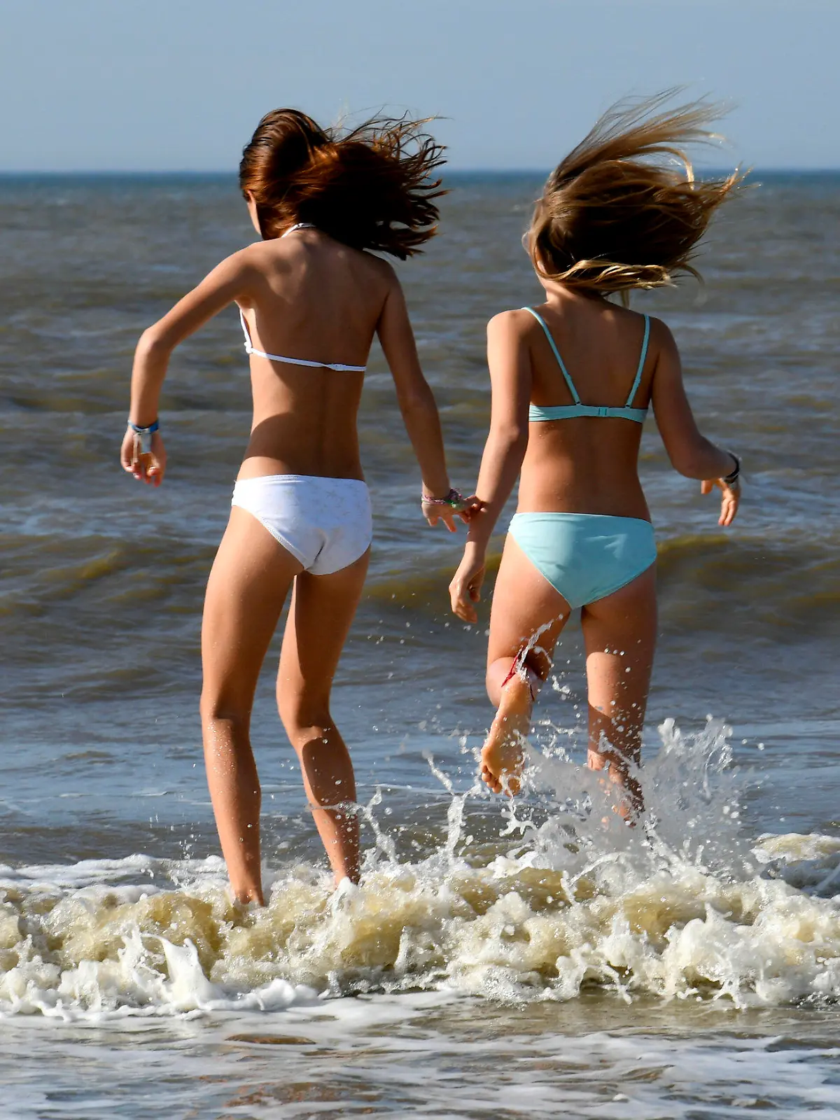 13.10.2018, Niederlande, Bloemendaal An Zee: Zwei Mädchen springen bei sonnigem Wetter am Strand über Wellen der Nordsee. Foto: Ina Fassbender/dpa +++ dpa-Bildfunk +++
