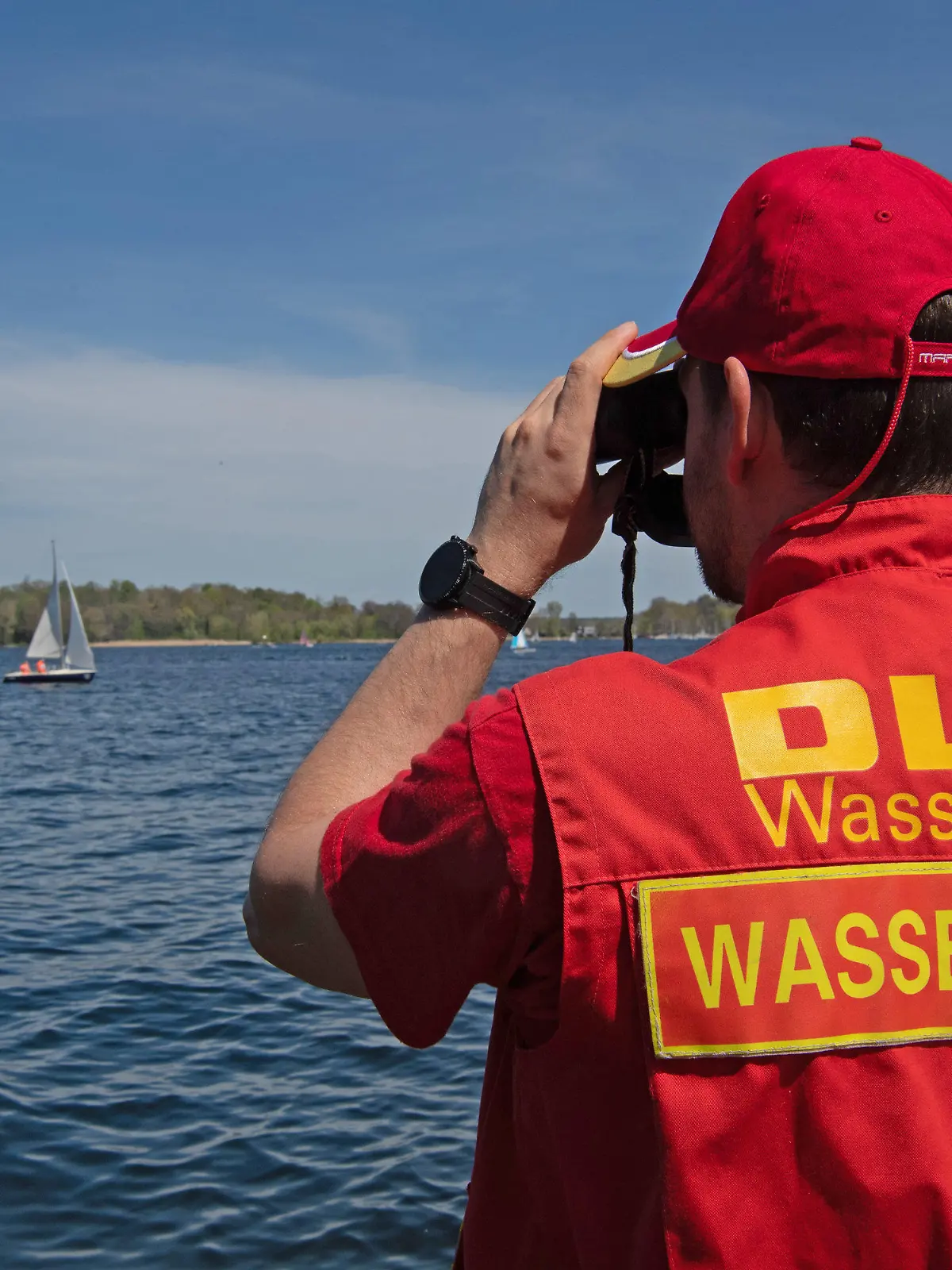 09.05.2021, Berlin: Ein Mitglied der Deutschen Lebensrettungs-Gesellschaft (DLRG) beobachtet die Boote auf dem Wannsee. Ein kurzes Sommerintermezzo kam quasi «über Nacht» und brachte Temperaturen bis zu 30 Grad. Foto: Paul Zinken/dpa +++ dpa-Bildfunk +++
