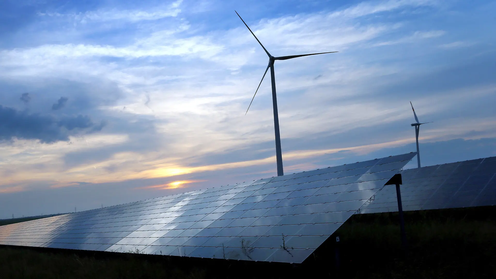 ARCHIV - 06.06.2018, Bayern, Kitzingen: Der mit Wolken überzogene Abendhimmel spiegelt sich auf den Solarzellen einer vor Windrädern stehenden Solarkraftanlage (zu «Bund Naturschutz fordert rasche und konsequente Klimaschutz-Maßnahmen»). Foto: Karl-Josef Hildenbrand/dpa +++ dpa-Bildfunk +++