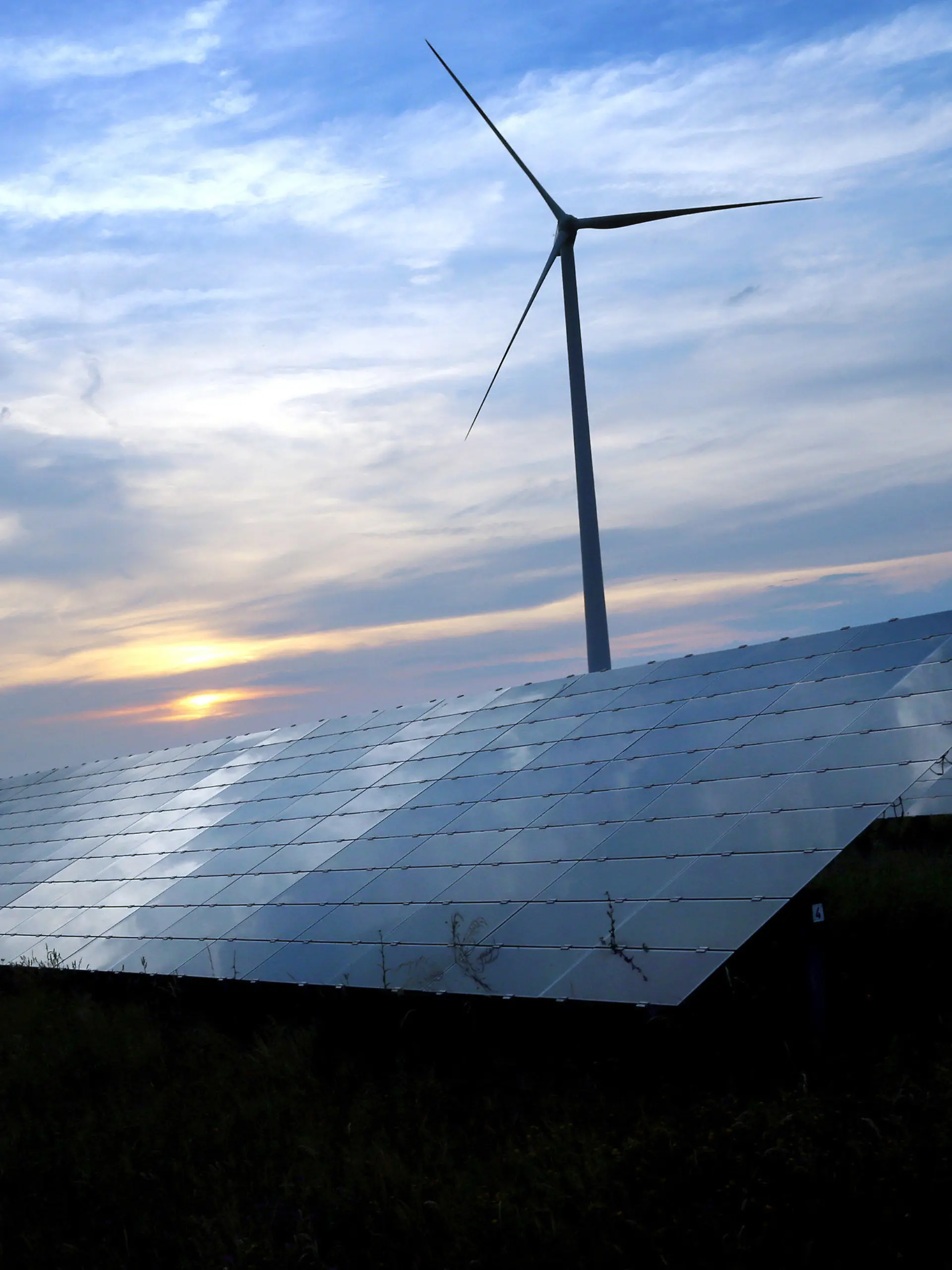 ARCHIV - 06.06.2018, Bayern, Kitzingen: Der mit Wolken überzogene Abendhimmel spiegelt sich auf den Solarzellen einer vor Windrädern stehenden Solarkraftanlage (zu «Bund Naturschutz fordert rasche und konsequente Klimaschutz-Maßnahmen»). Foto: Karl-Josef Hildenbrand/dpa +++ dpa-Bildfunk +++
