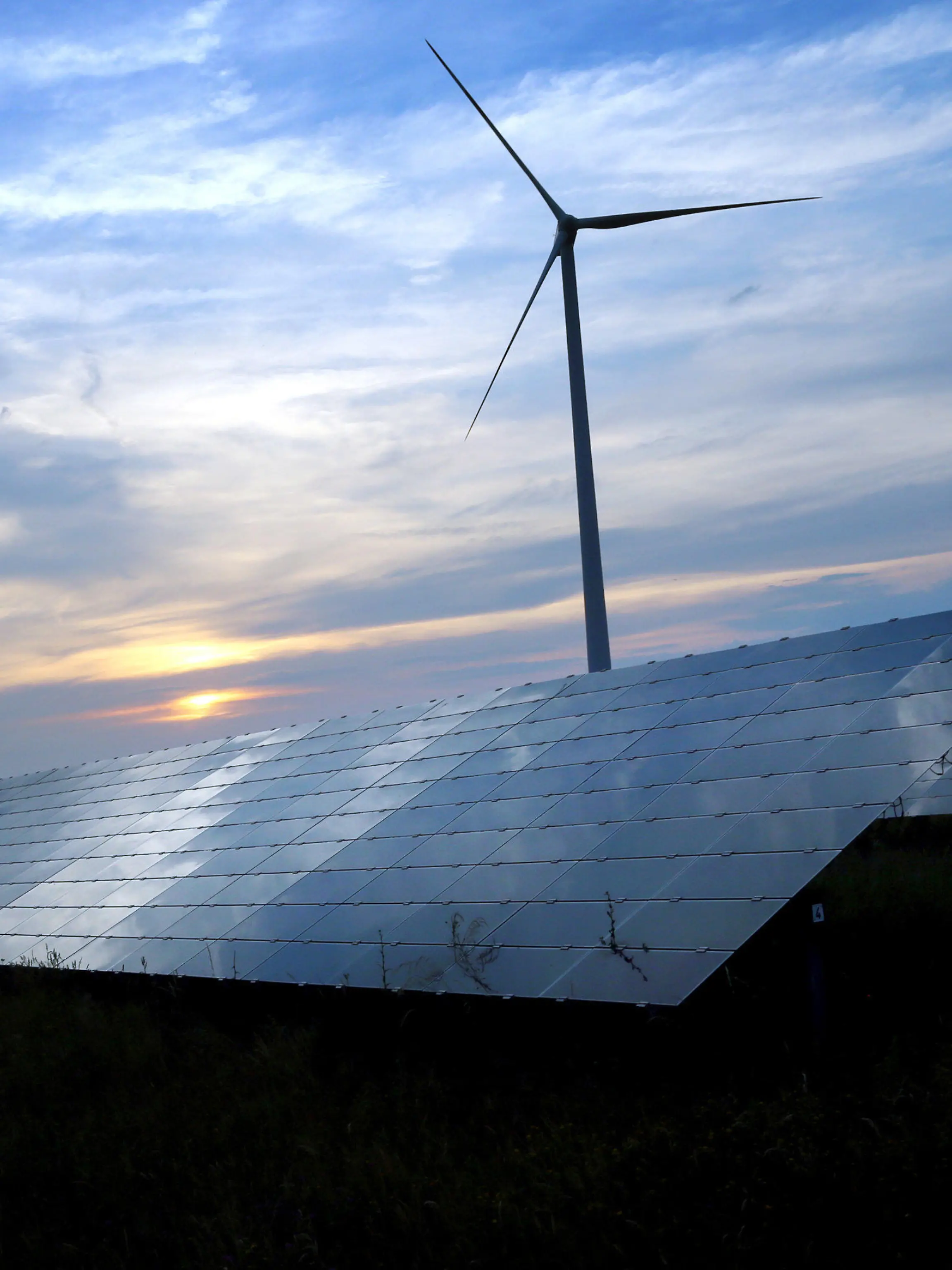 ARCHIV - 06.06.2018, Bayern, Kitzingen: Der mit Wolken überzogene Abendhimmel spiegelt sich auf den Solarzellen einer vor Windrädern stehenden Solarkraftanlage (zu «Bund Naturschutz fordert rasche und konsequente Klimaschutz-Maßnahmen»). Foto: Karl-Josef Hildenbrand/dpa +++ dpa-Bildfunk +++