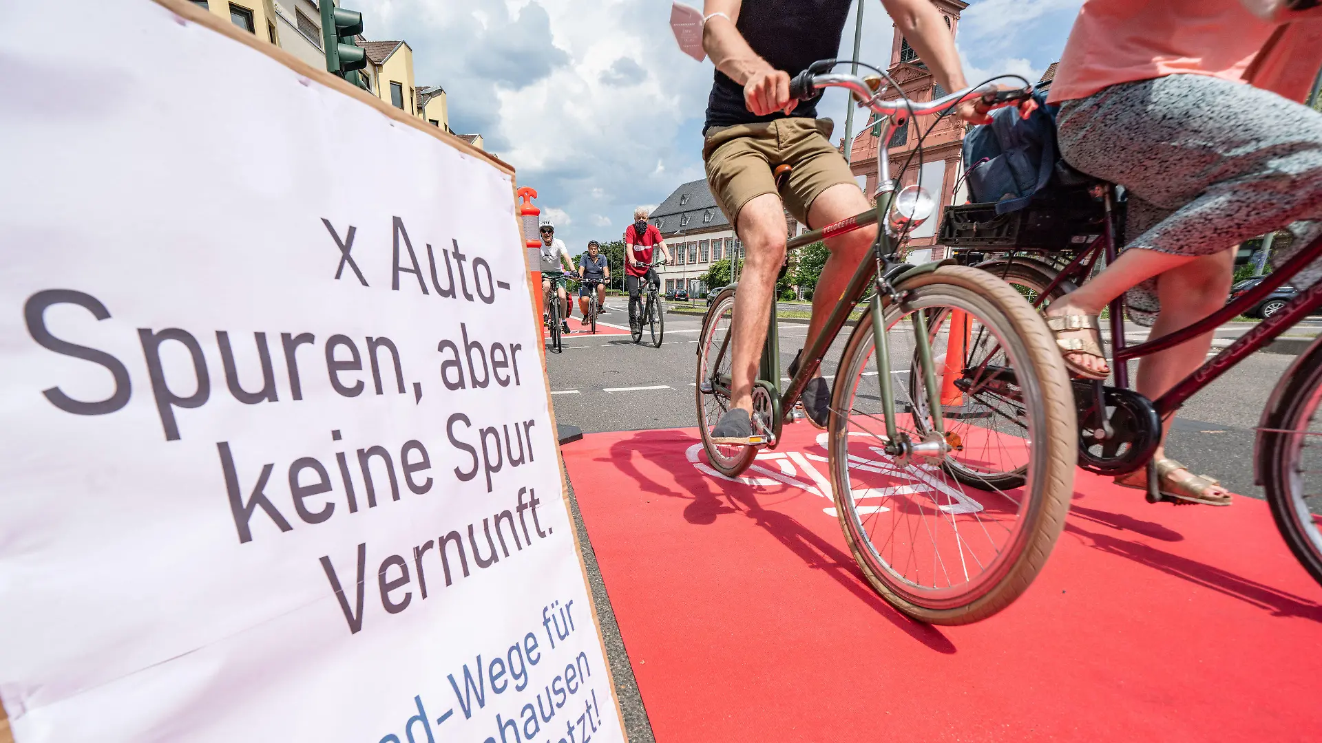 03.06.2021, Hessen, Frankfurt/Main: Aktivisten rollen auf der Walter-Kolb-Straße im Stadtteil Sachsenhausen auf einem roten Teppich als «Pop-Up-Radweg», der zuvor ausgelegt worden war. Auf einem Plakat links steht «x Auto-Spuren, aber keine Spur Vernunft». Mit Aktionen in mehreren hessischen Städten haben Fahrradinitiativen am Weltfahrradtag für mehr Radwege demonstriert. Foto: Frank Rumpenhorst/dpa/Frank Rumpenhorst/dpa +++ dpa-Bildfunk +++