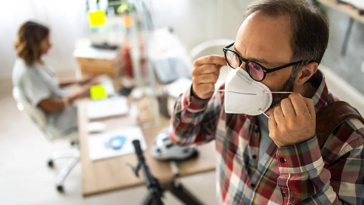 Mann setzt im Büro Maske auf