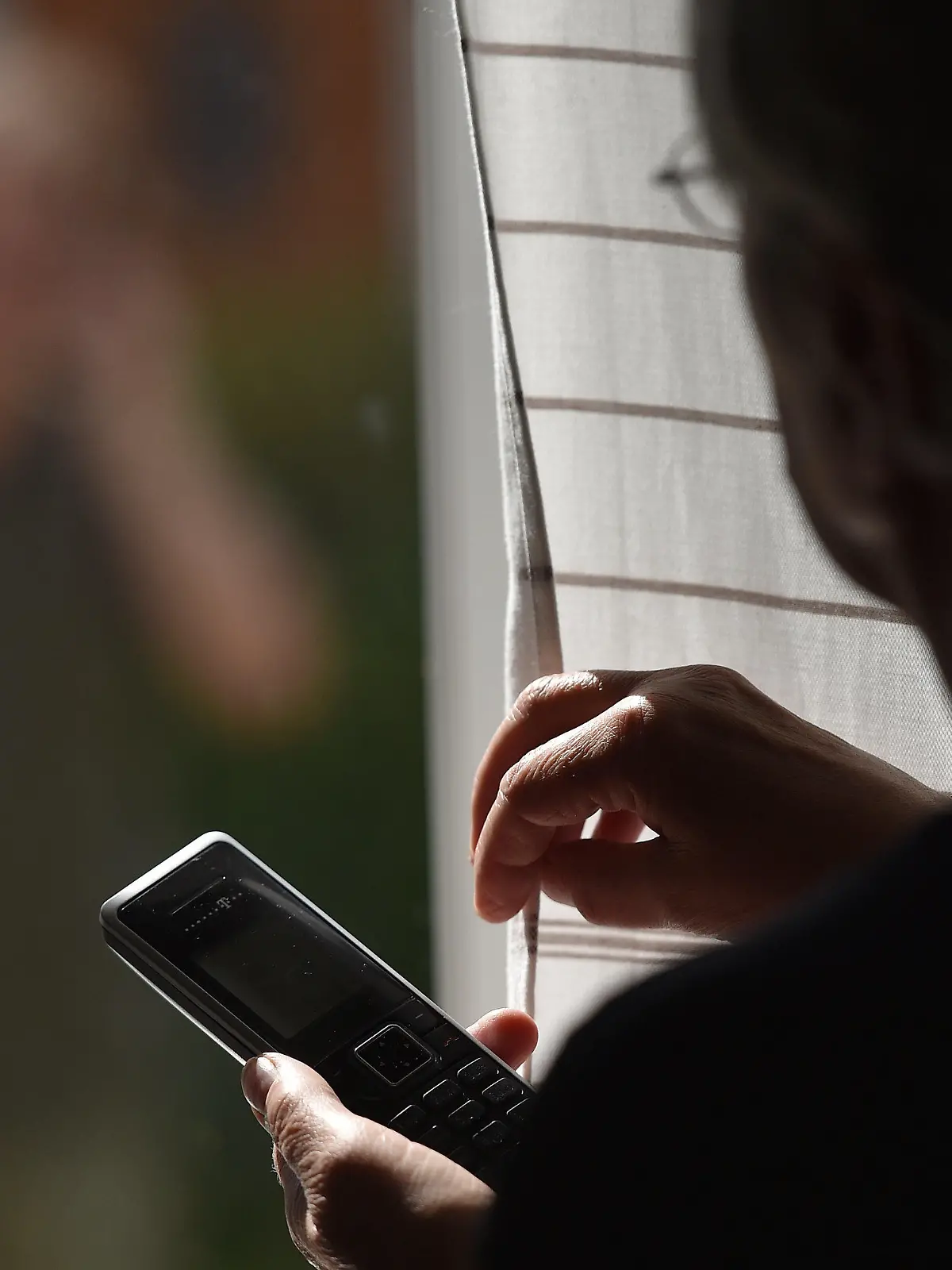 ARCHIV - ILLUSTRATION - 05.07.2016, Bayern, Garmisch-Partenkirchen: Eine Frau steht mit einem Telefon am Fenster, vor dem ein Mann steht (gestellte Szene). Vor zehn Jahren erhitzte in Berlin ein Hilfsangebot für Stalker die Gemüter. Heute ist diese Arbeit im Sinn des Opferschutzes anerkannt. Doch inzwischen suchen mehr Opfer als Täter Rat. (zu "Bilanz - zehn Jahre Hilfsangebote für Stalker in Berlin" vom 03.05.2018) Foto: Angelika Warmuth/dpa +++ dpa-Bildfunk +++
