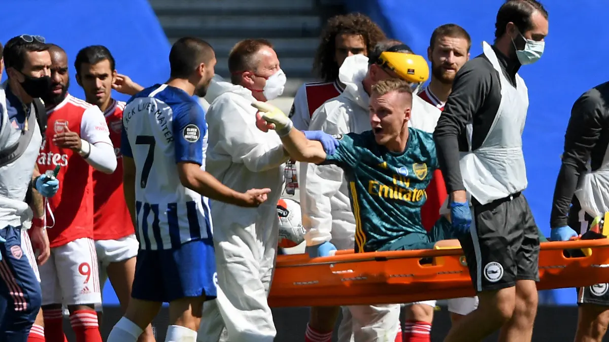 20.06.2020, Großbritannien, Brighton: Fußball: Premier League, England, Brighton & Hove Albion - FC Arsenal, 30. Spieltag, Amex Stadion: Der Torwart Bernd Leno (3.v.r) vom FC Arsenal zeigt auf Neal Maupay (4.v.l) von Brighton & Hove Albion, während er auf einer Trage vom Feld getragen wird. Foto: Mike Hewitt/Nmc Pool/PA Wire/dpa +++ dpa-Bildfunk +++