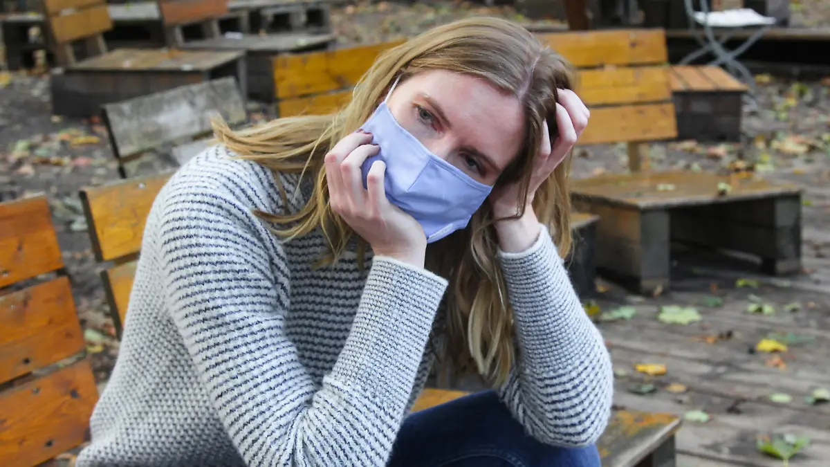 Junge Frau sitzt mit Maske im Park