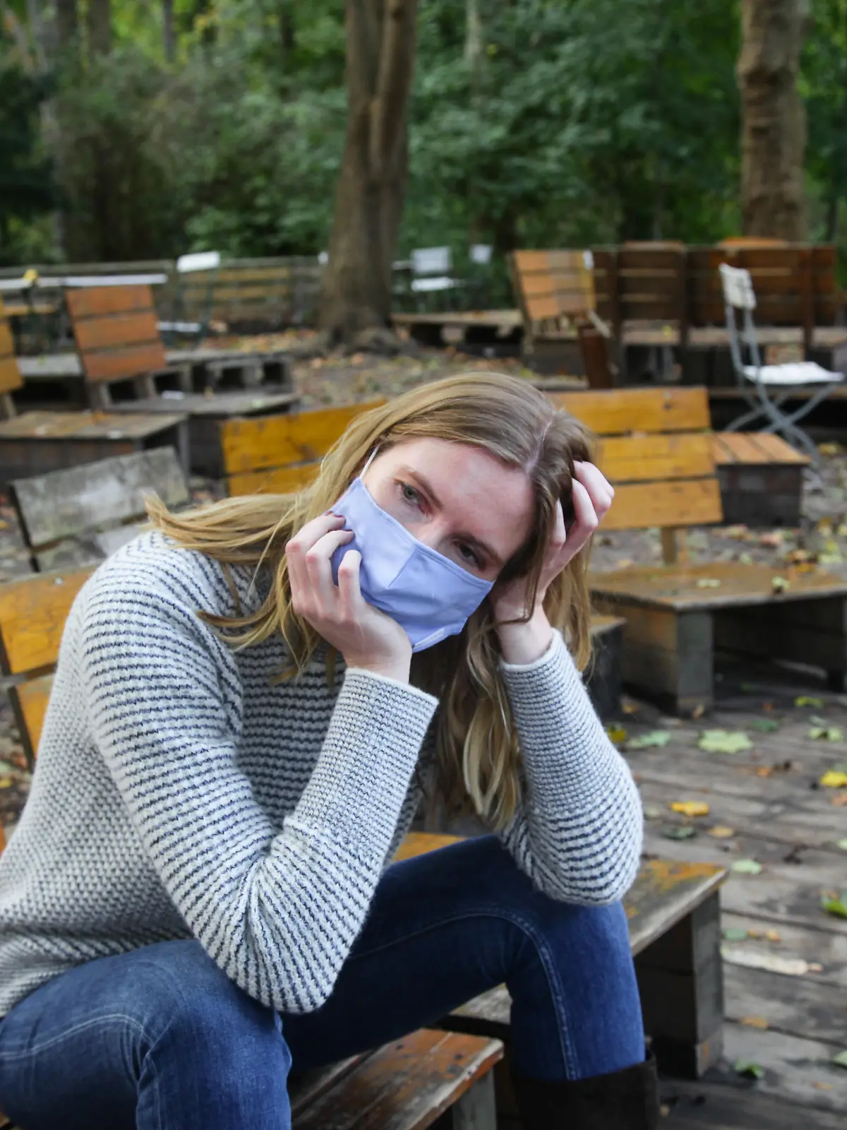 Junge Frau sitzt mit Maske im Park