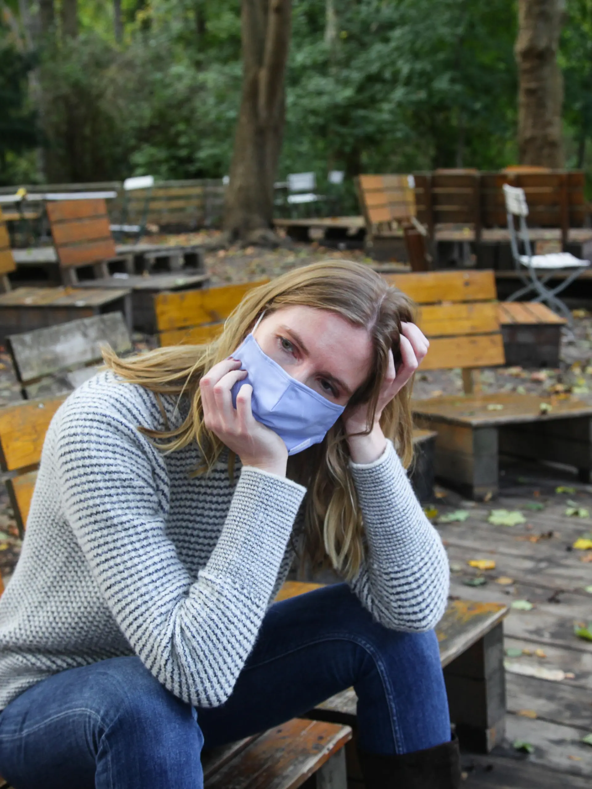 Junge Frau sitzt mit Maske im Park