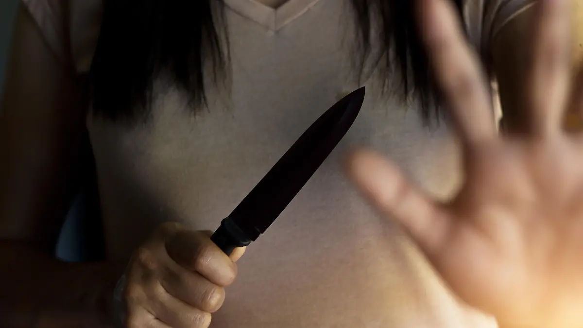 Woman holding a knife in hand while defending herself from attacks.