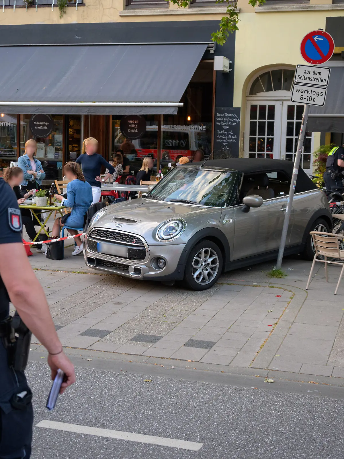 02.06.2021, Hamburg: Ein Polizist steht vor dem Unfallauto, das zwischen Fahrrädern, Tischen, Stühlen und zerstörtem Geschirr steht. Ein Mann ist mit einem Leihauto rückwärts in den Außenbereich eines Restaurants in Hamburg gefahren. Vier Menschen seien leicht verletzt worden, sagte ein Polizeisprecher. Foto: Jonas Walzberg/dpa - ACHTUNG: Autokennzeichen und Privatpersonen gepixelt +++ dpa-Bildfunk +++
